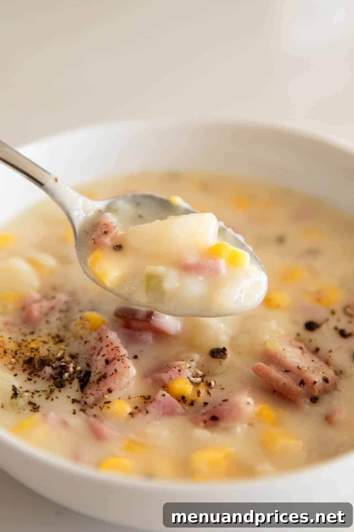 Hearty Slow Cooker Ham and Potato Chowder 11 A white bowl with slow cooker ham and potato soup with a spoon above holding a spoonful of it.