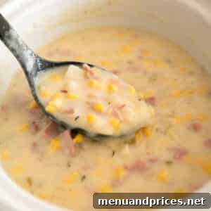 Slow cooker ham and potato soup with corn in a white bowl with a black spoon.
