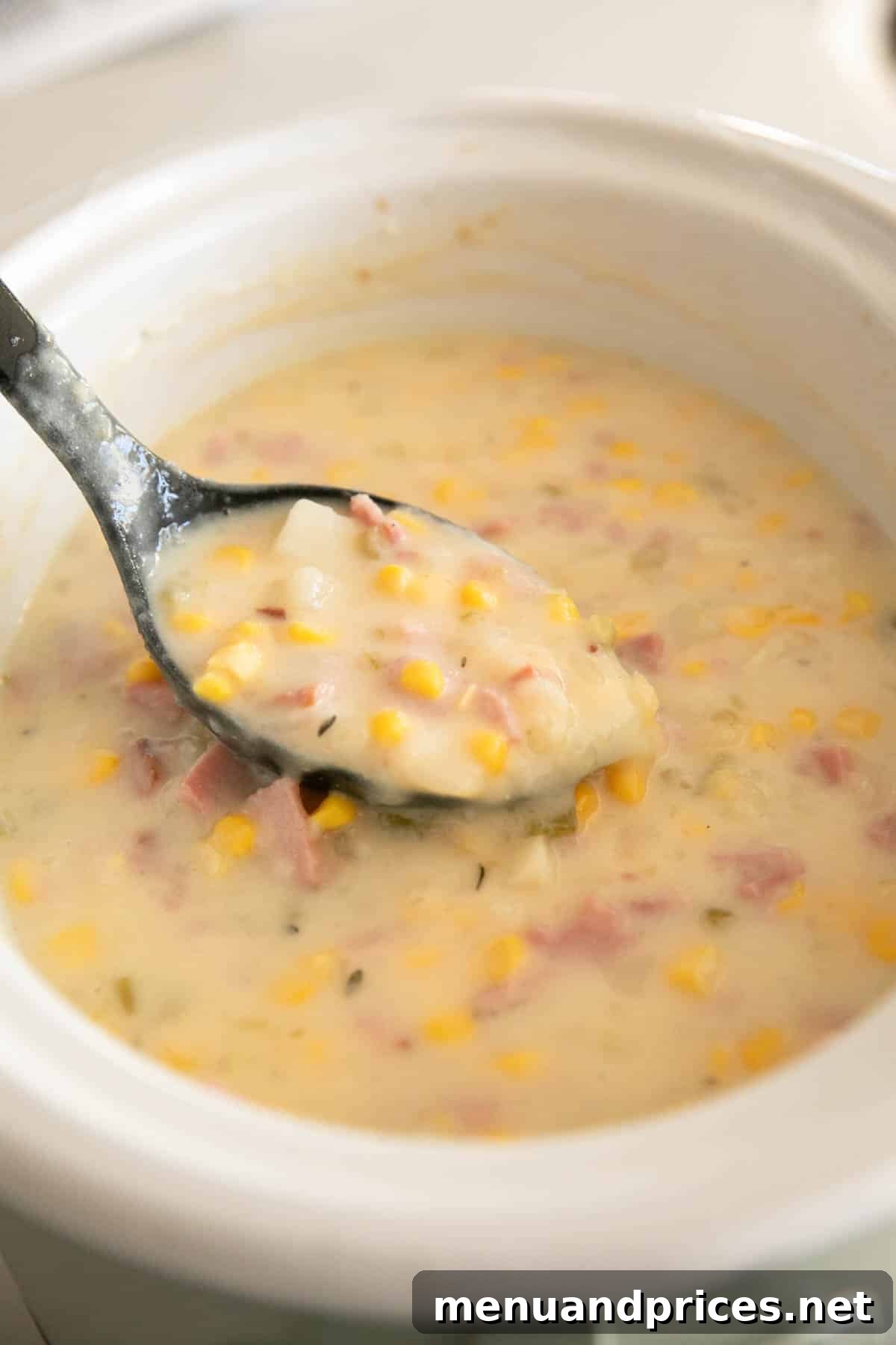 Hearty Slow Cooker Ham and Potato Chowder 3 Slow cooker ham and potato soup with corn in a white bowl with a black spoon.