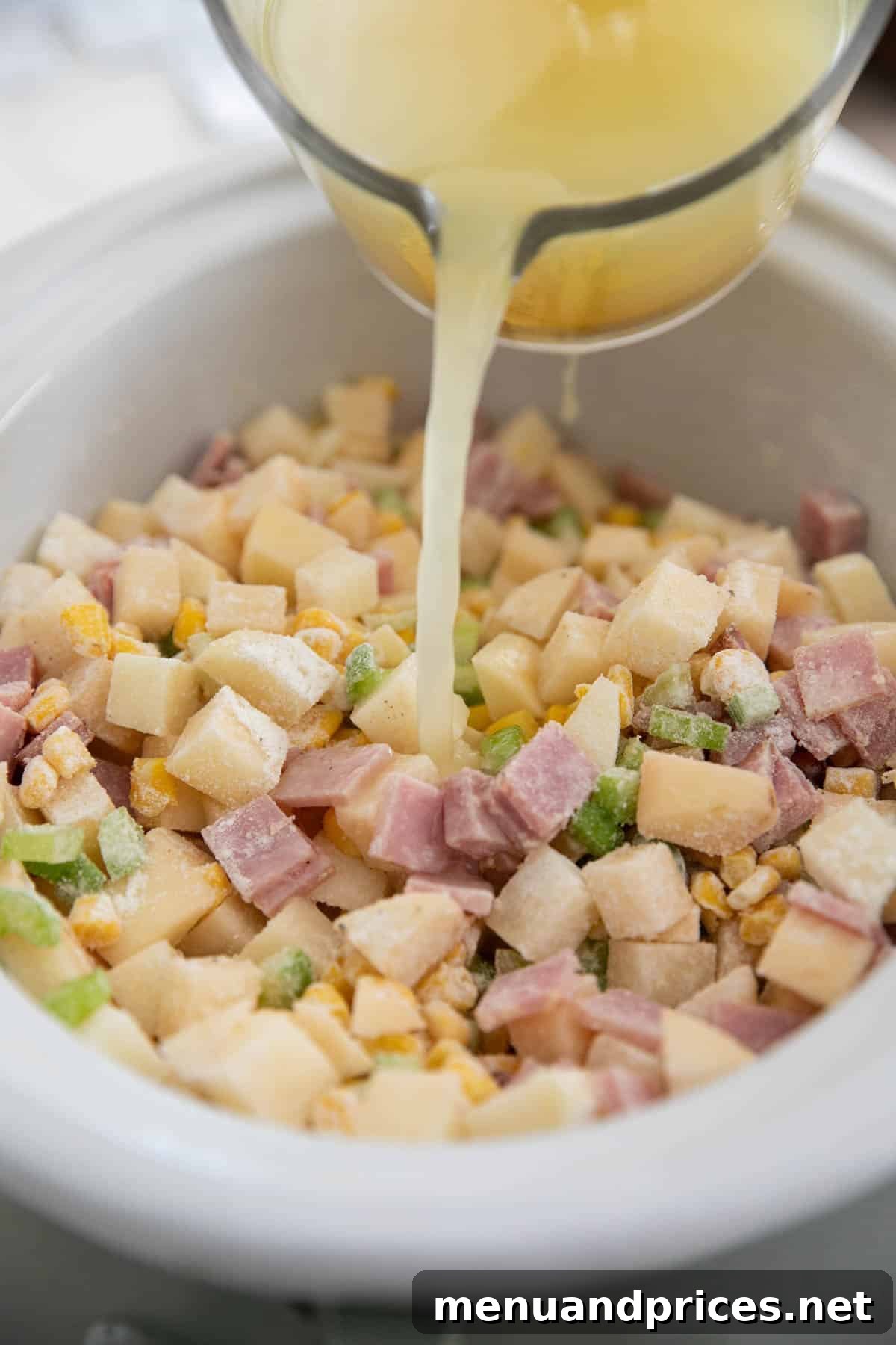 Hearty Slow Cooker Ham and Potato Chowder 6 Chicken broth being poured from a glass measuring cup into the slow cooker ham and potato soup.