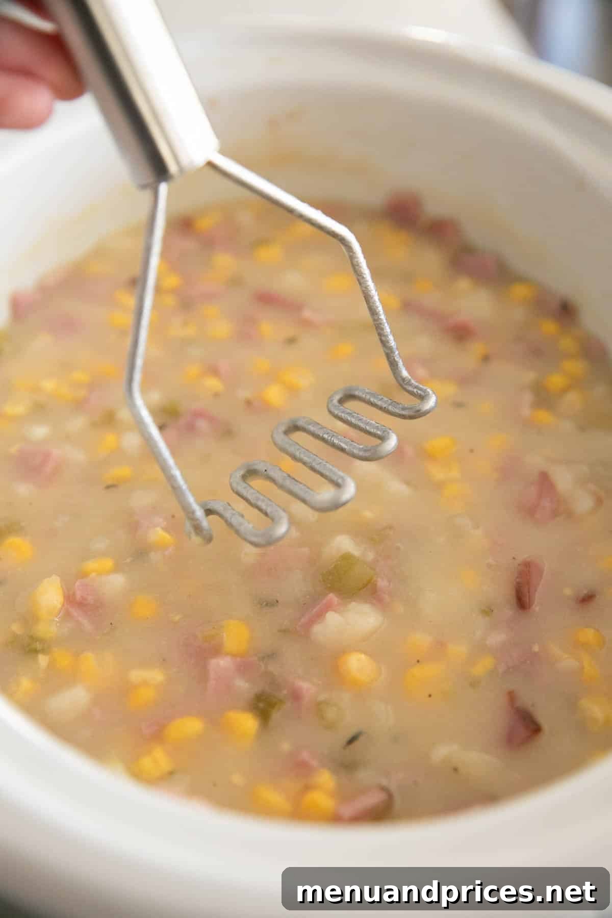 Hearty Slow Cooker Ham and Potato Chowder 8 A potato masher is being used to mash the potatoes in the slow cooker ham and potato soup.
