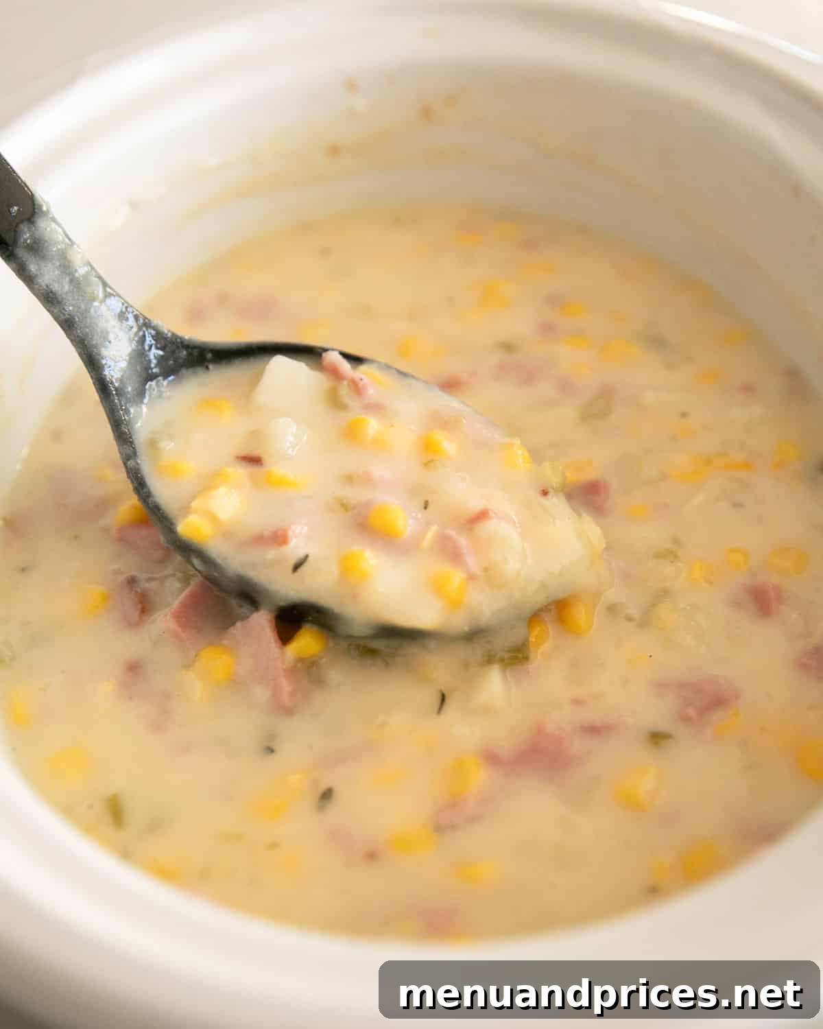 Hearty Slow Cooker Ham and Potato Chowder 10 A black spoon is ladling some of the slow cooker ham and potato soup.