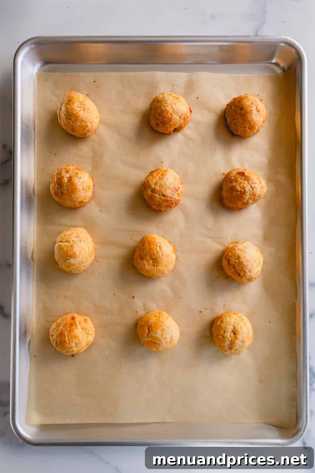 Fluffy Havarti Cheese Gougères 11 A close-up of freshly baked golden cheese puffs on a baking sheet, ready to be transferred to a cooling rack.