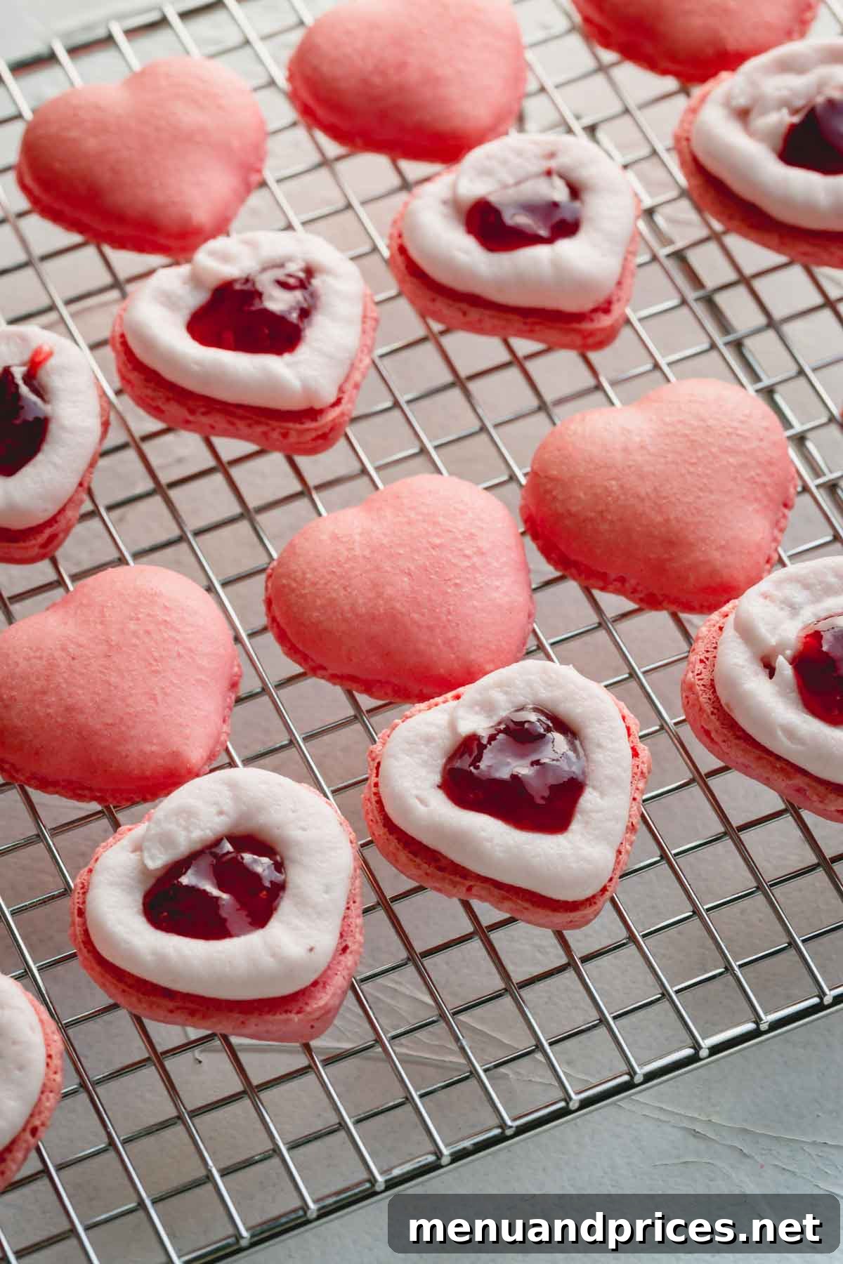Pink macaron shells with a delicate piped buttercream border and a dollop of strawberry jam in the center, ready for assembly.