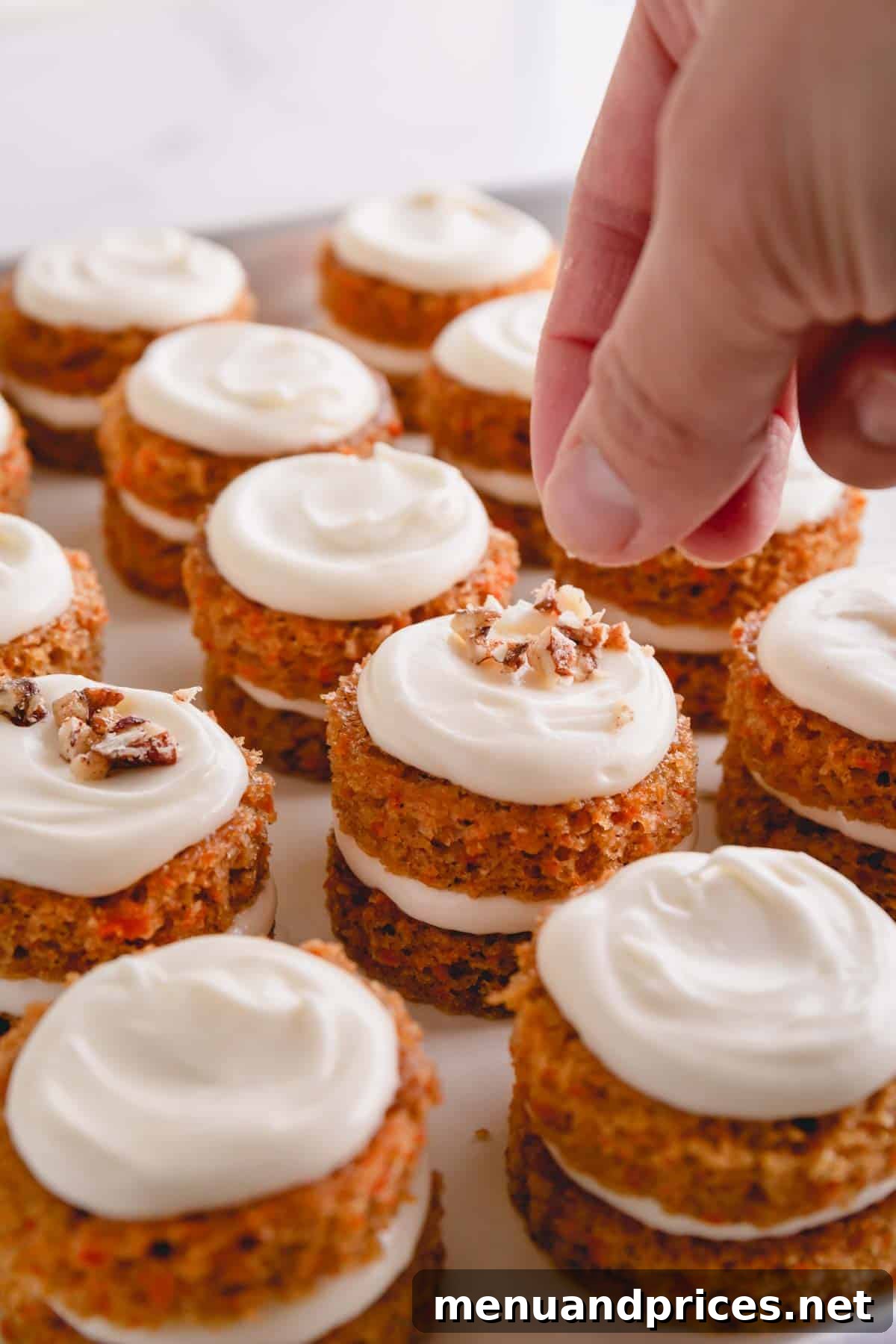 A close-up shot of a hand sprinkling crunchy candied pecans on freshly frosted mini carrot cakes, adding the final touch.