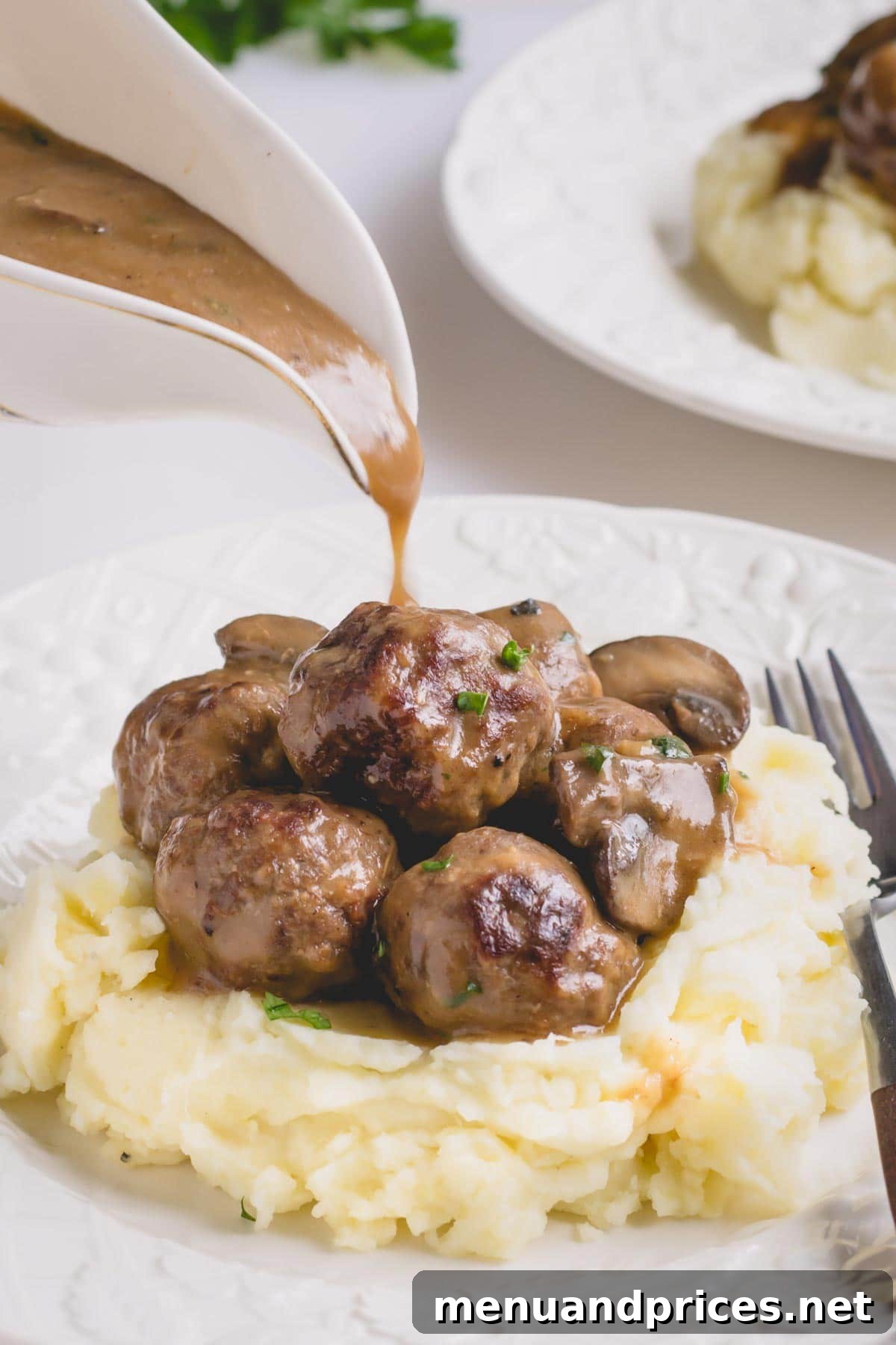 Brown gravy pouring over the meatballs and mashed potatoes on a white plate, highlighting the rich texture and appealing presentation.