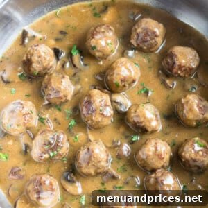 Close-up of a perfectly formed beef meatball in mushroom gravy, garnished with fresh herbs.