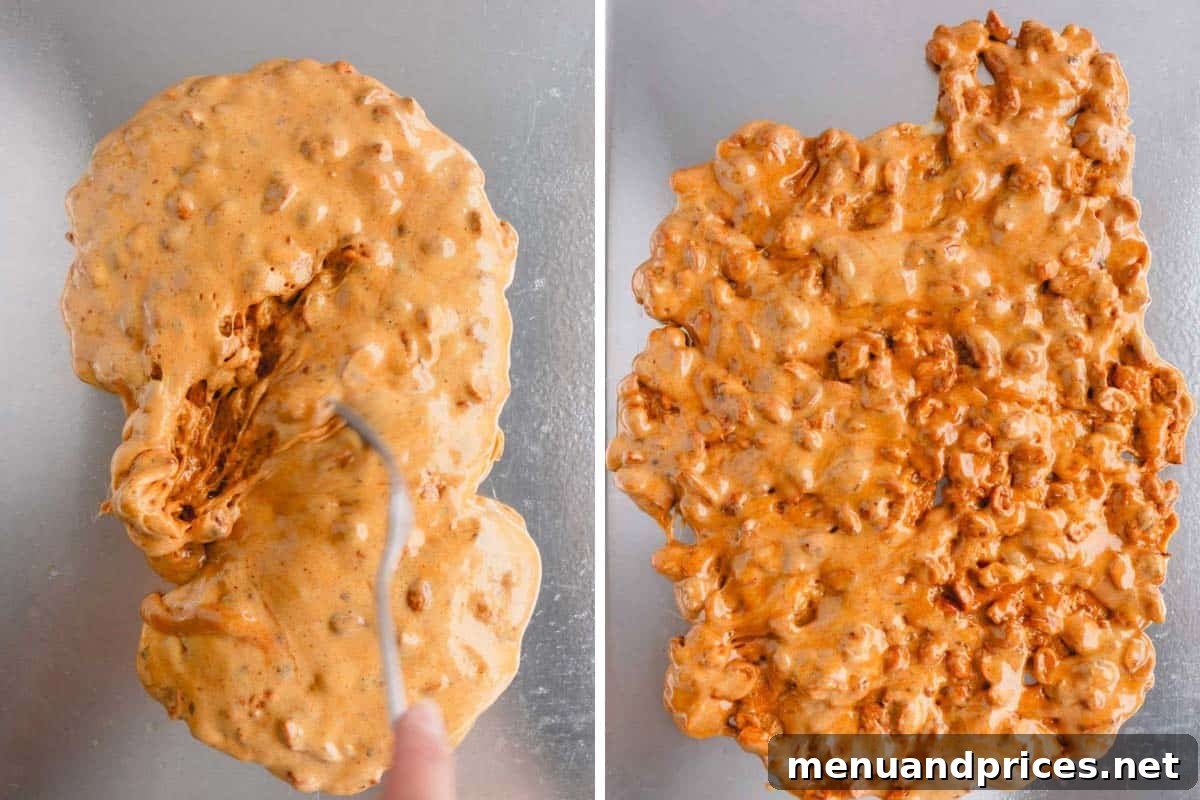 A hot peanut brittle mixture being carefully spread into an even layer over a baking sheet using two forks.