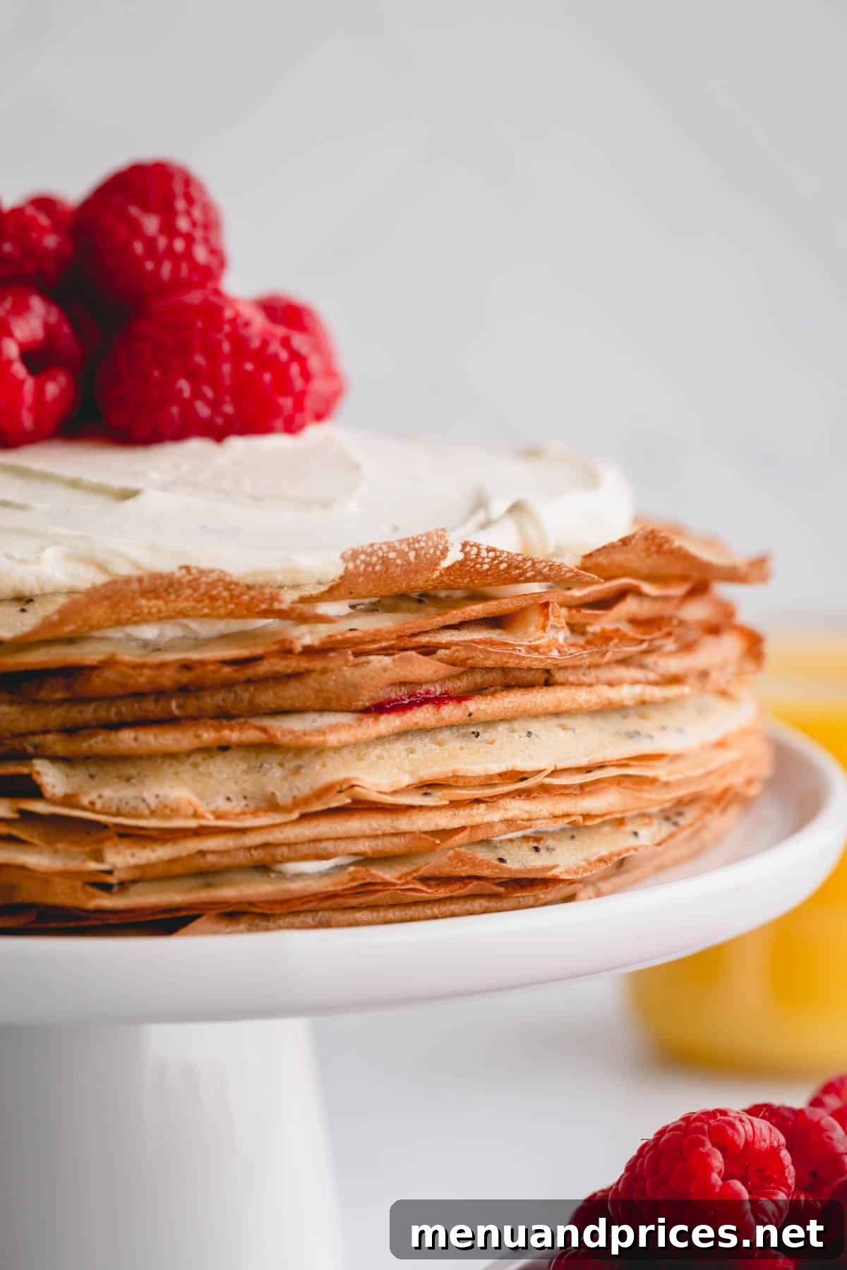 Zesty Lemon Raspberry Crepe Tower 2 A beautifully assembled lemon raspberry crepe cake, adorned with fresh whipped cream and vibrant red raspberries on top, ready to be served.