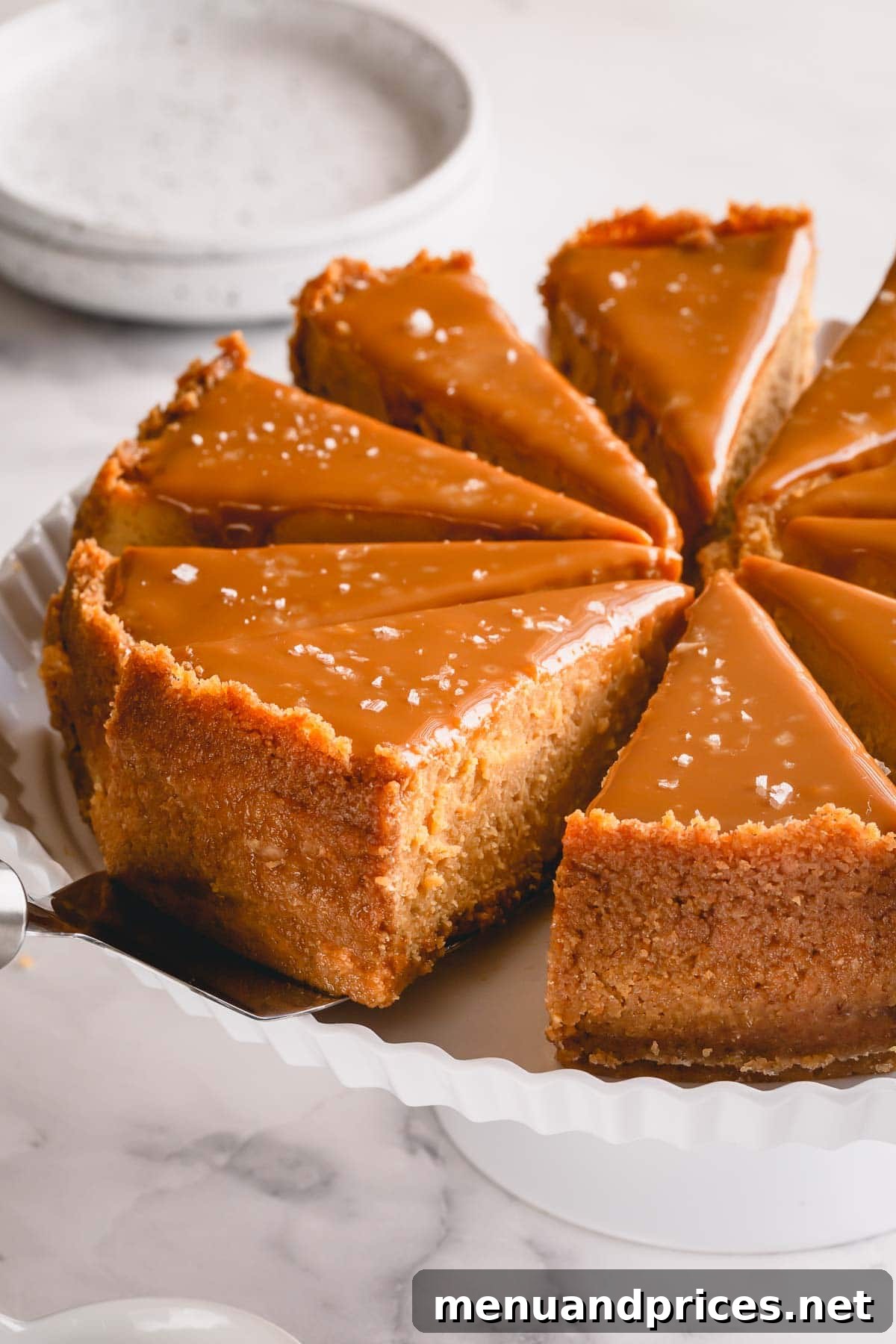 Sliced Dulce de Leche Cheesecake on a white serving platter, perfectly smooth with a golden topping and flaky sea salt.
