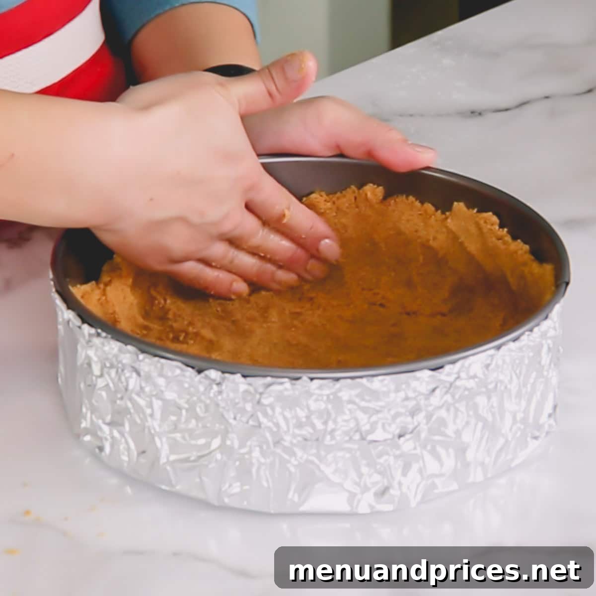 Detailed shot of graham cracker crust being evenly spread and pressed into a springform pan.