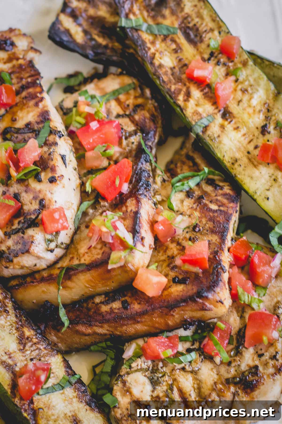 Flame-Grilled Swordfish Steaks 4 Two perfectly grilled swordfish steaks, garnished with fresh herbs and diced tomatoes, resting on a white plate, ready to be served.