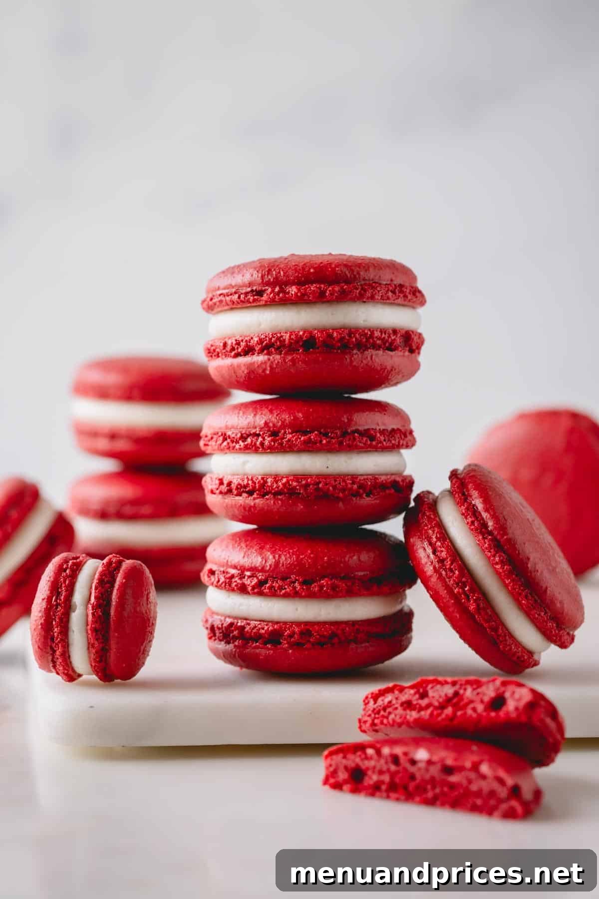 3 red velvet macarons stacked on top of each other and surrounded with more macarons, showcasing their vibrant red color and creamy white filling.