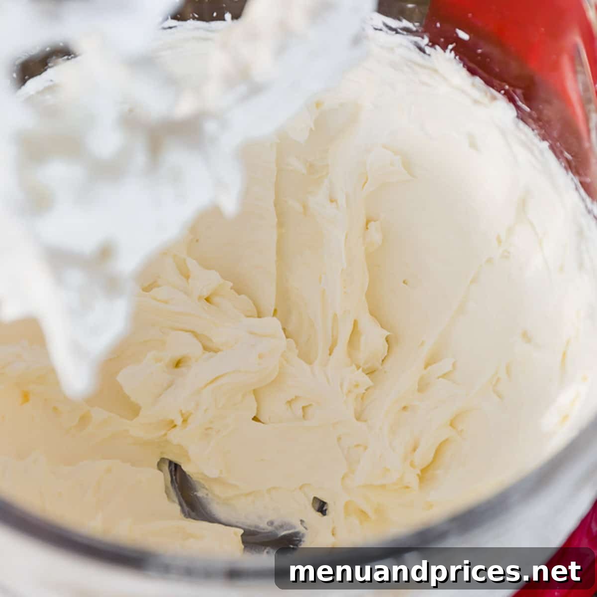 Whipped cream cheese in a glass bowl of a stand mixer, ready for frosting.