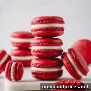 3 red velvet macarons stacked on top of each other and surrounded with more macarons.