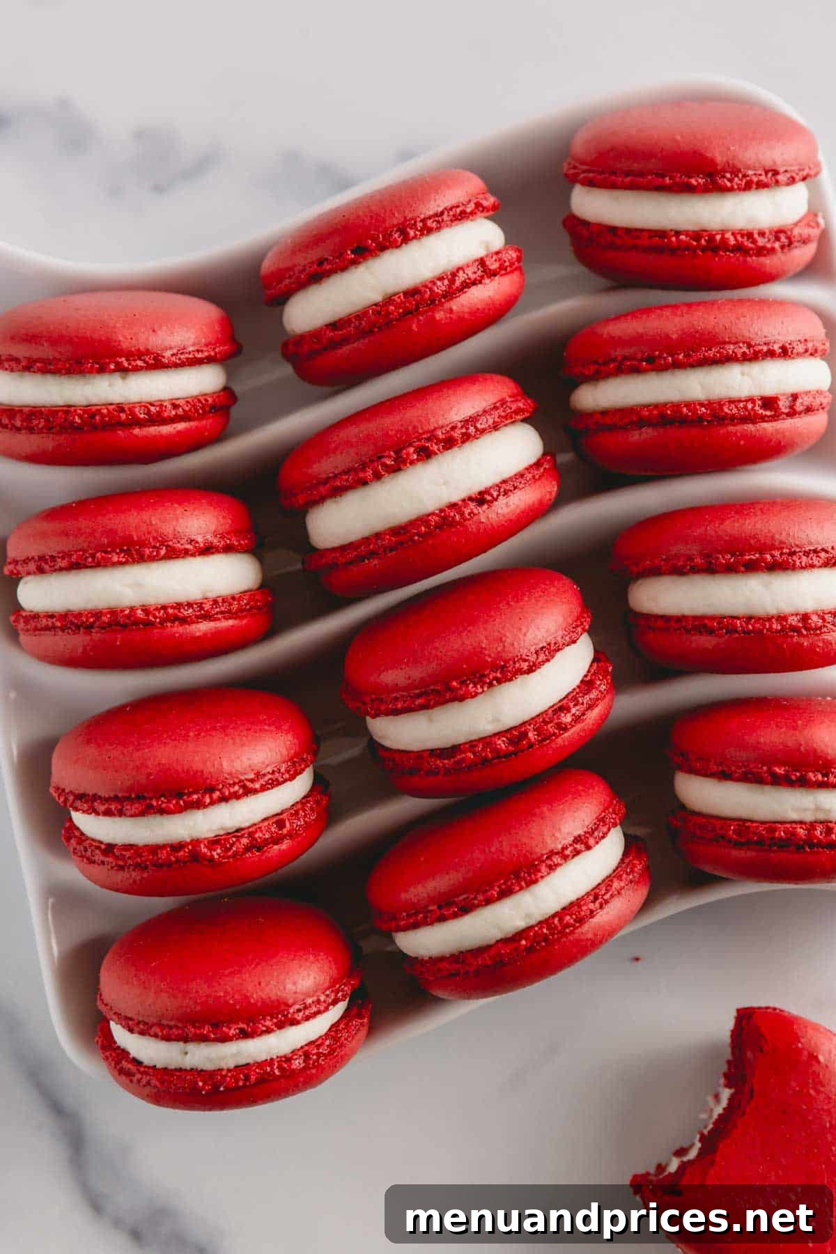 Vibrant red velvet macarons filled with white cream cheese frosting arranged on a white serving platter, showing perfect 'feet'.