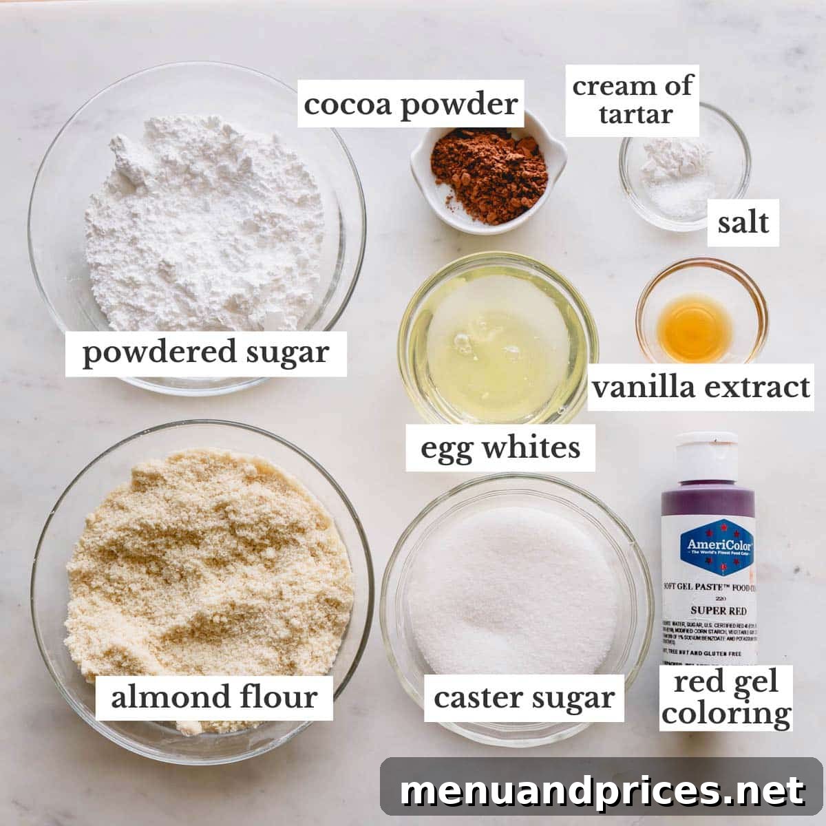 Red velvet macarons ingredients in individual bowls, including egg whites, almond flour, powdered sugar, cocoa powder, granulated sugar, and red gel food coloring.