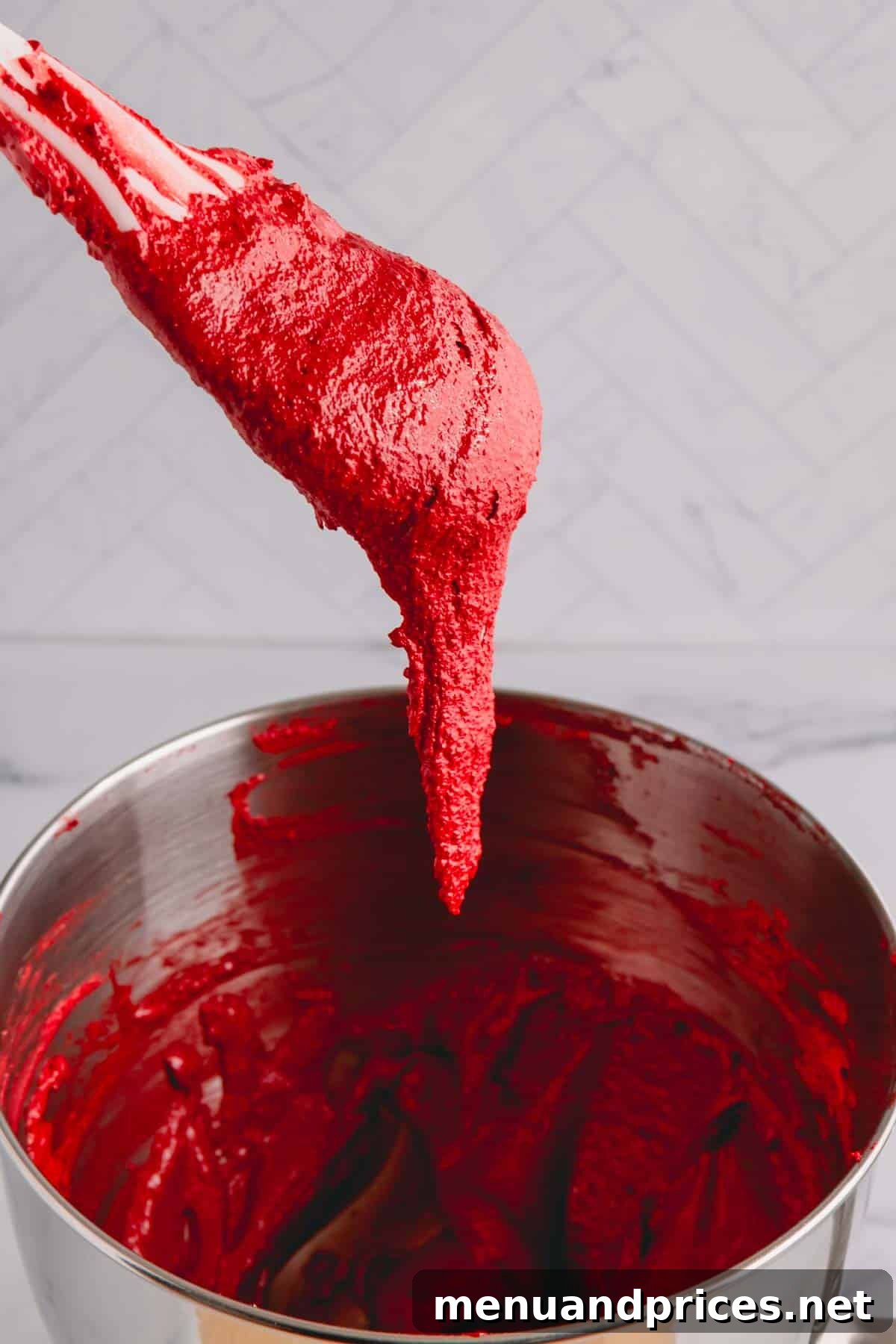 A spoonful of red macaron batter falling off the spatula into the mixing bowl, illustrating the 'lava-like' consistency.