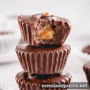 A bitten chocolate cup with exposed caramel filling stacked on top of 2 chocolate cups.