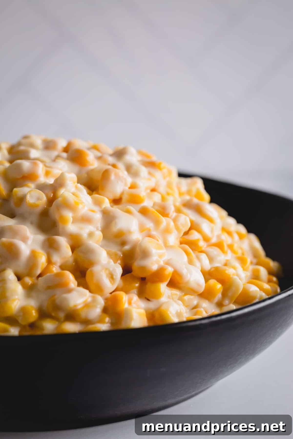 Effortless Creamed Corn 2 A black bowl of creamed corn, garnished for serving.