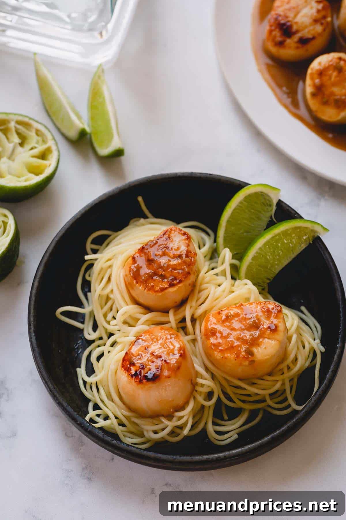 Tequila Lime Glazed Scallop Pasta 2 Three perfectly seared scallops resting over a bed of fine spaghetti, elegantly garnished with fresh lime wedges, highlighting the dish's vibrant flavors and appealing presentation.