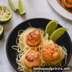 3 seared scallops over a bed of spaghetti and garnished with lime wedges.