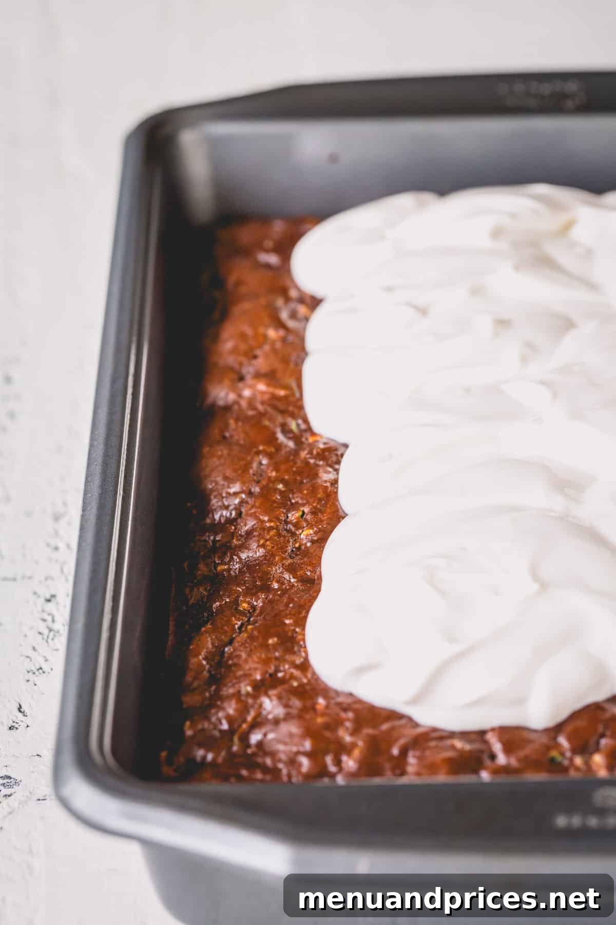 Fudgy Chocolate Zucchini Sheet Cake 8 Chocolate zucchini cake in a pan with generous dollops of sour cream frosting scooped on top, ready to be spread.