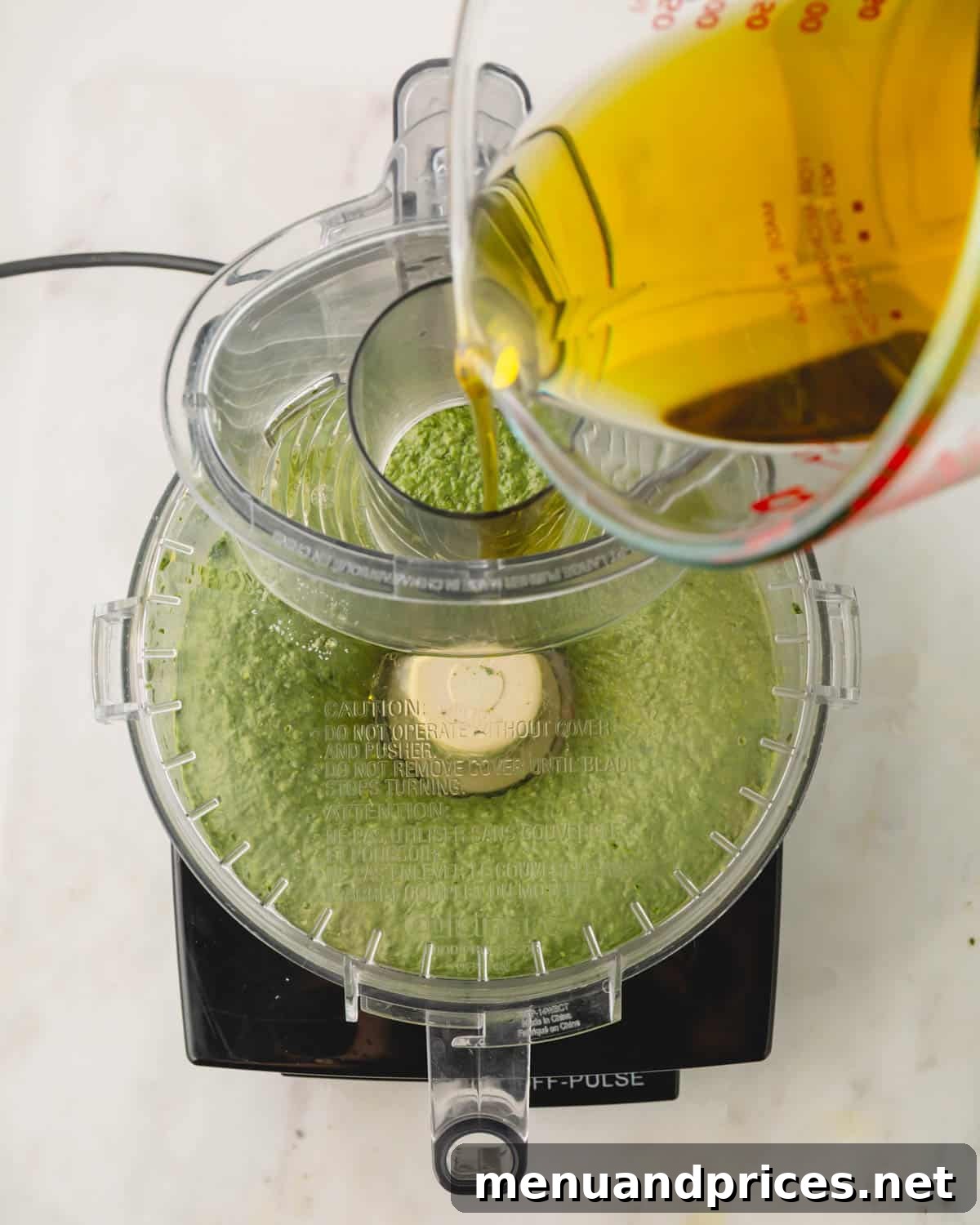 Big Batch Basil Pesto: A Freezer-Friendly Recipe 11 Olive oil slowly drizzling into the food processor while the basil mixture is processing, creating an emulsion.