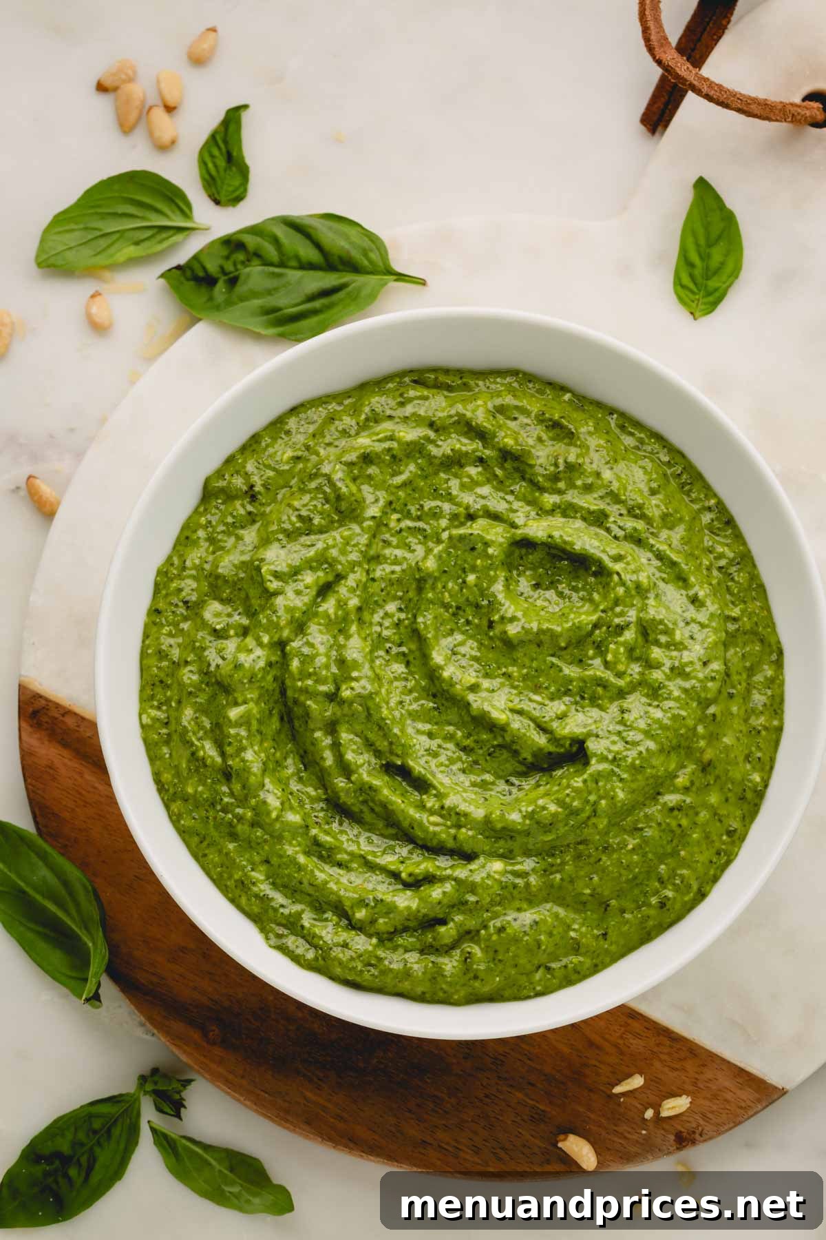 Big Batch Basil Pesto: A Freezer-Friendly Recipe 14 A beautifully arranged white bowl of large batch basil pesto on a serving platter, surrounded by fresh basil leaves and toasted pine nuts, ready for serving.