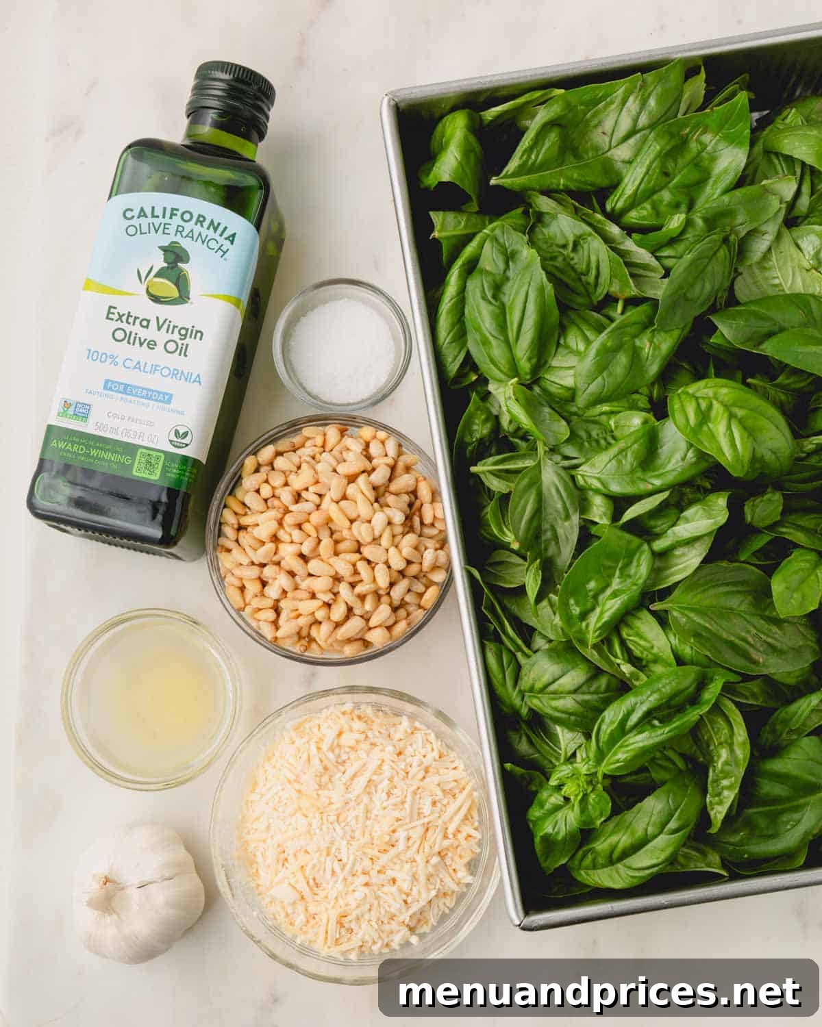 Big Batch Basil Pesto: A Freezer-Friendly Recipe 4 A flat lay of all the fresh ingredients for basil pesto: basil leaves, Parmesan cheese block, pine nuts, olive oil, garlic cloves, lemon, and a small bowl of salt.