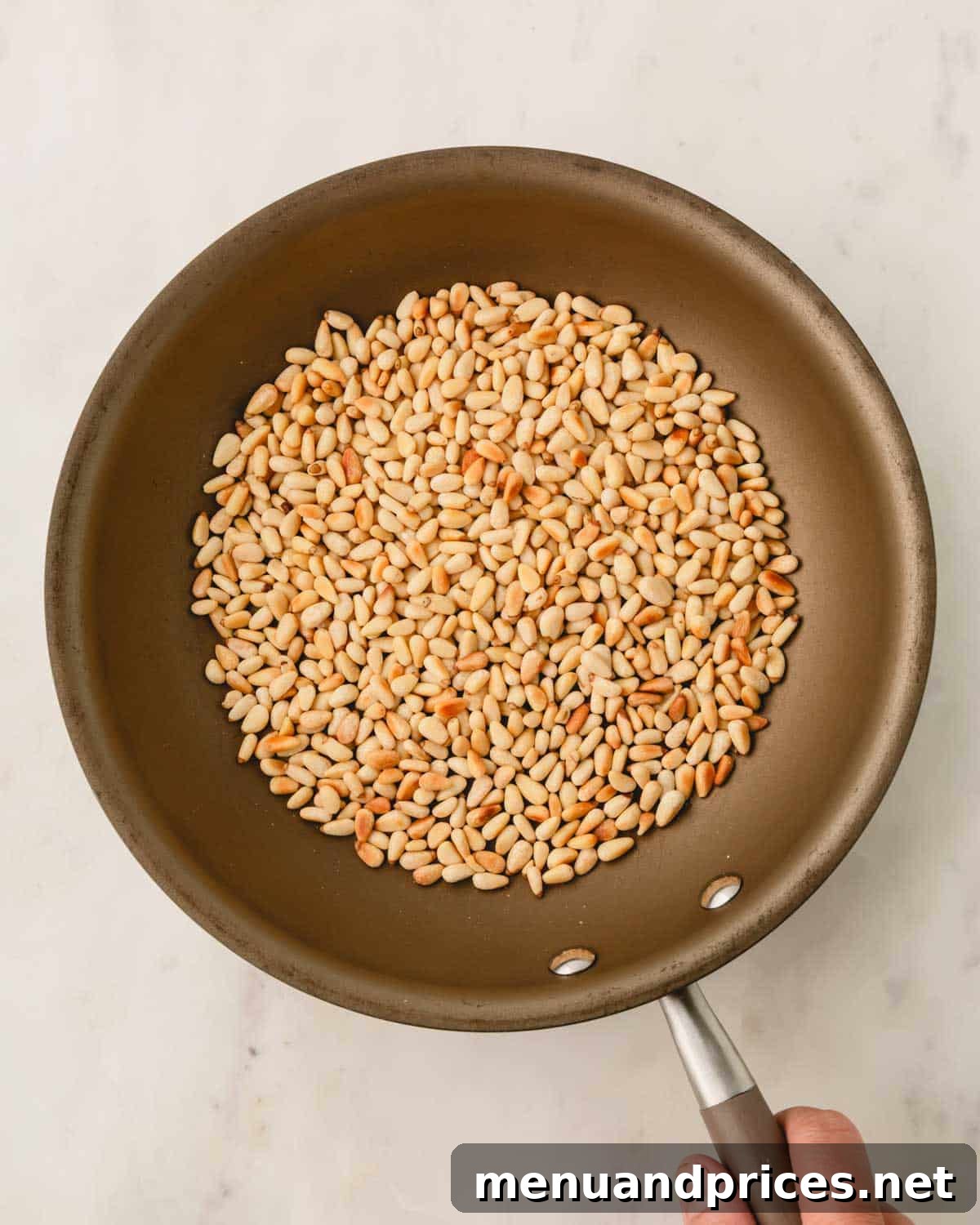 Big Batch Basil Pesto: A Freezer-Friendly Recipe 7 A hand stirring pine nuts in a medium skillet, highlighting the toasting process.