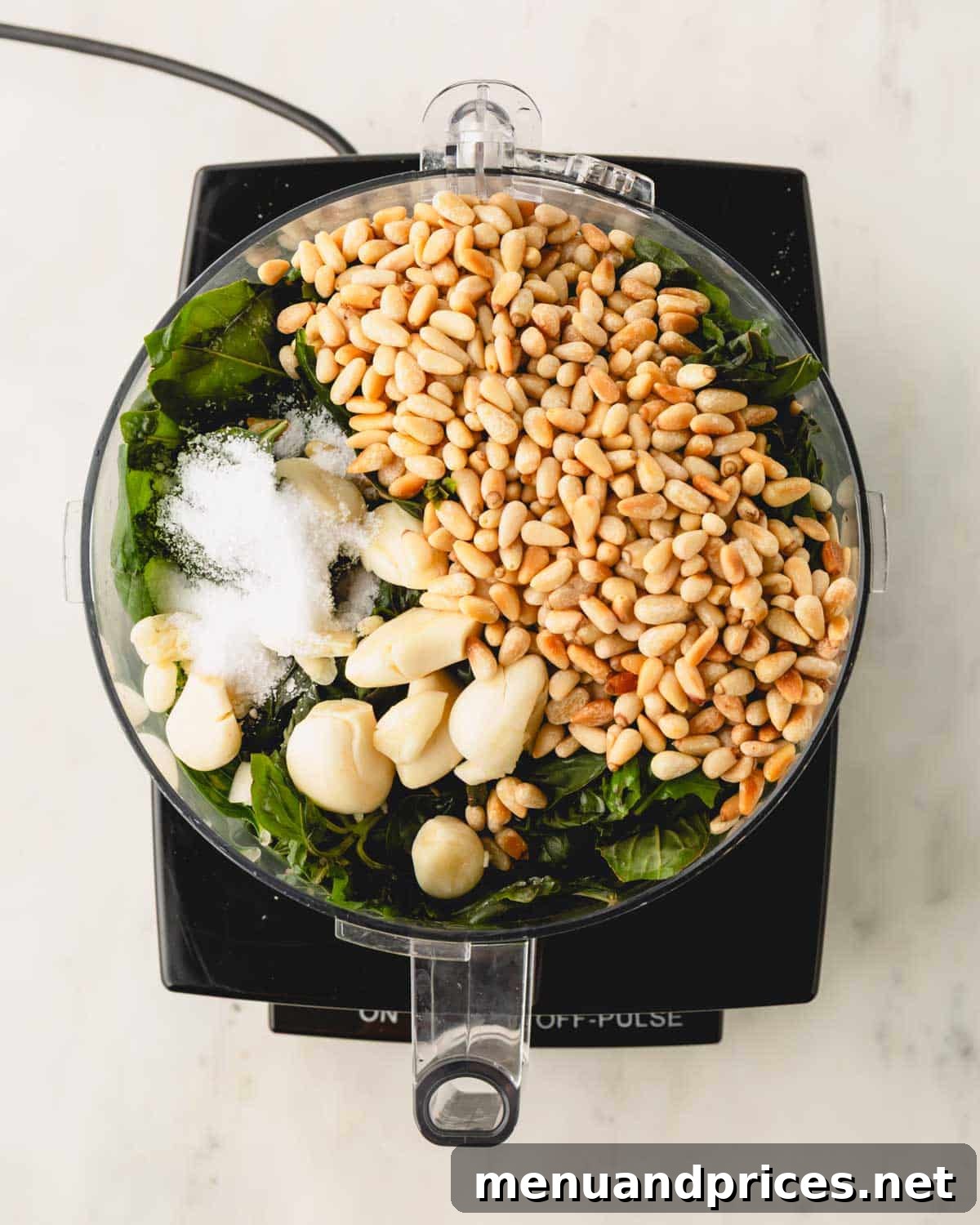 Big Batch Basil Pesto: A Freezer-Friendly Recipe 9 Frozen basil leaves, toasted pine nuts, garlic, and salt inside a food processor bowl, before blending.