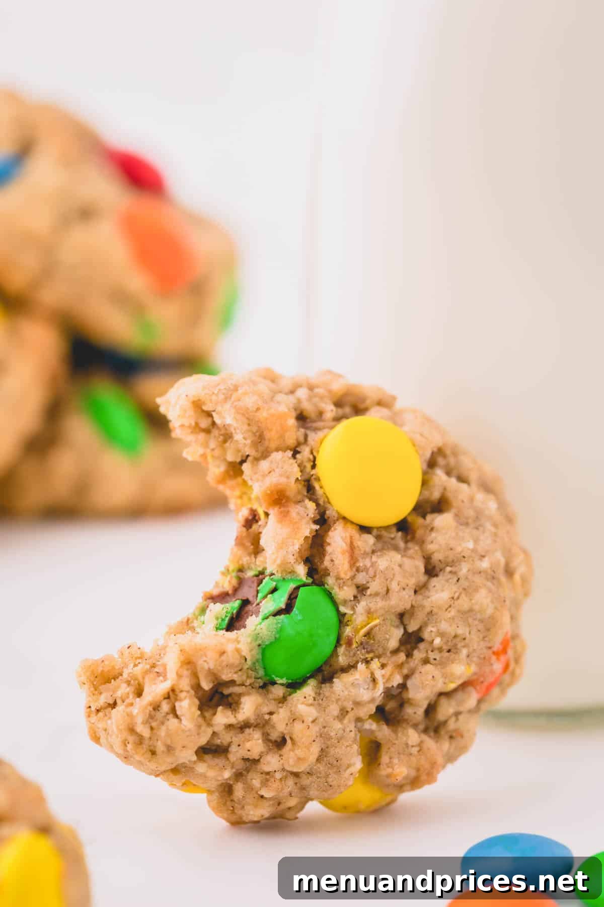 A close-up of a single apple cinnamon instant oatmeal cookie with a bite taken out, revealing its soft, chewy interior filled with oats and specks of apple and cinnamon.