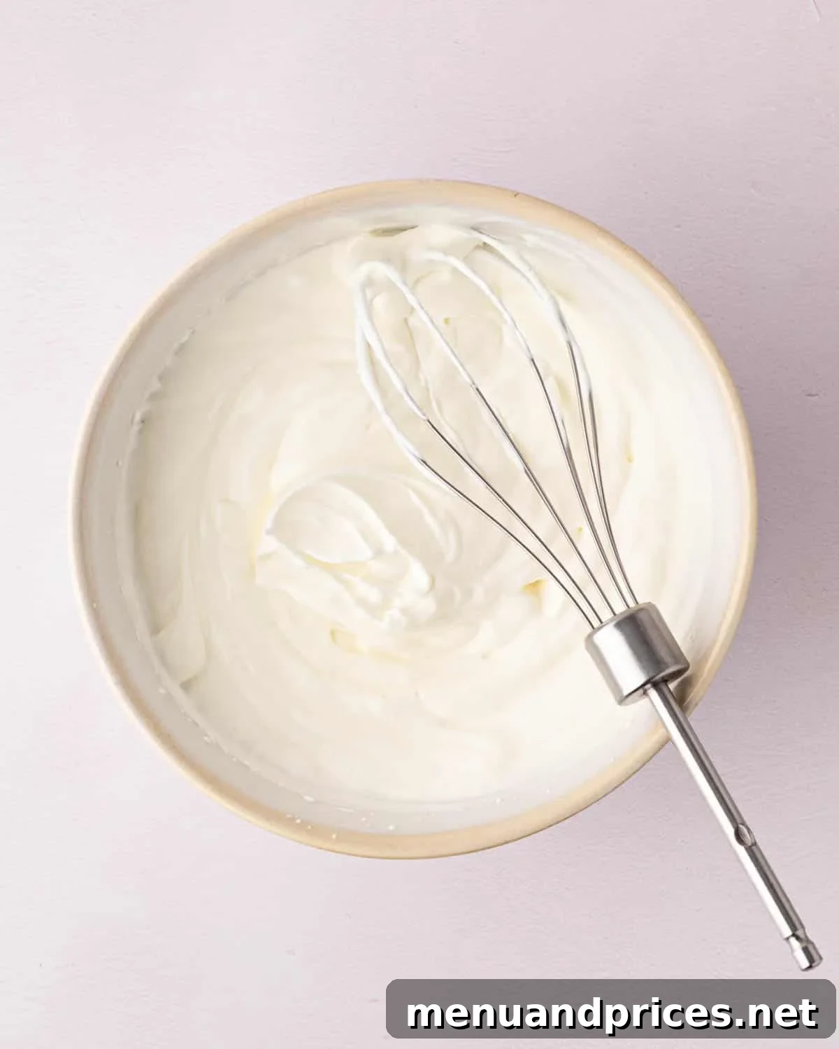 Zesty Lemon Dream 11 Whipped cream in a white bowl with a beater resting on the side.