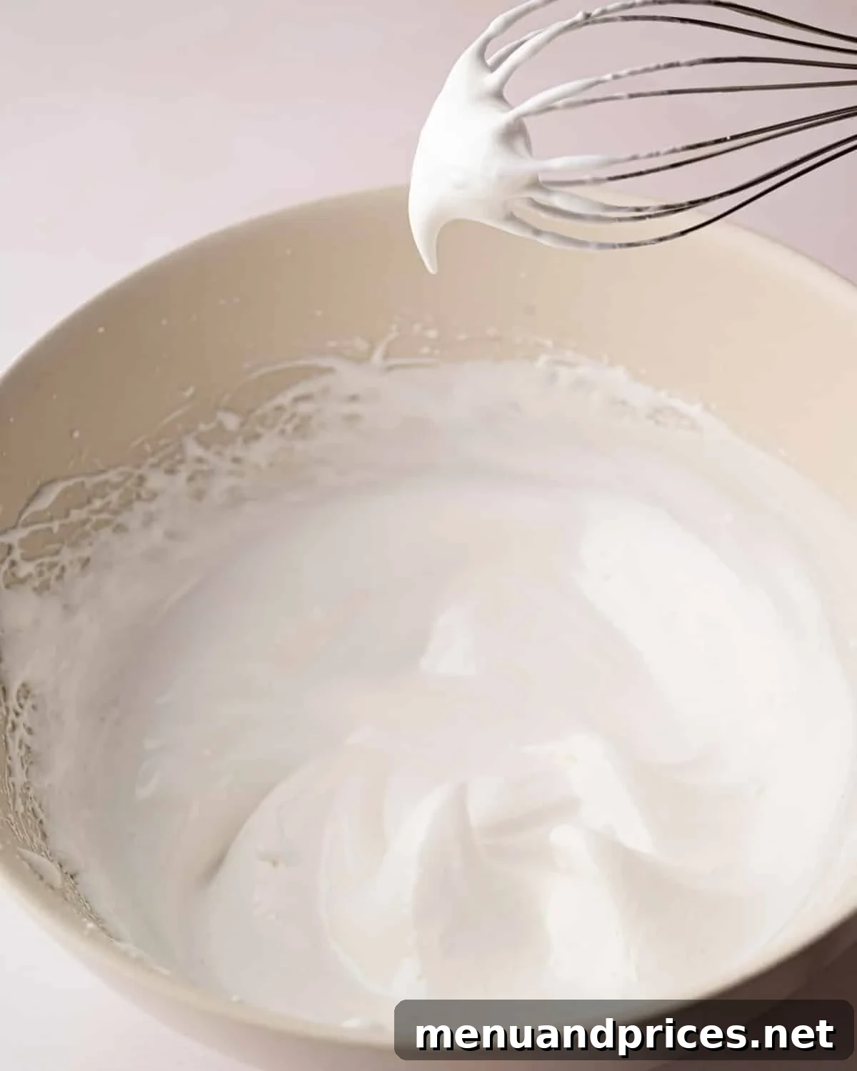 Zesty Lemon Dream 14 A white bowl with whipped egg whites with sugar and a hand mixer sitting on the side.