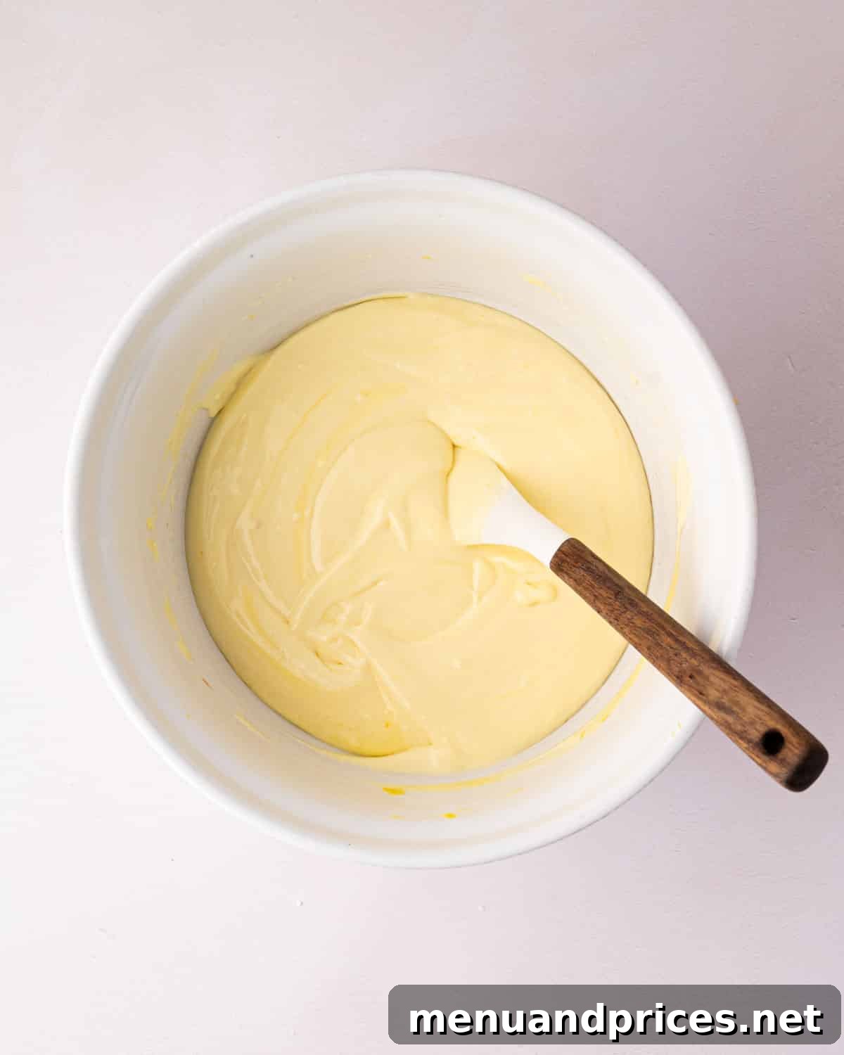 Zesty Lemon Dream 16 A white bowl with lemon mousse before it's set. A spatula is resting on the side.