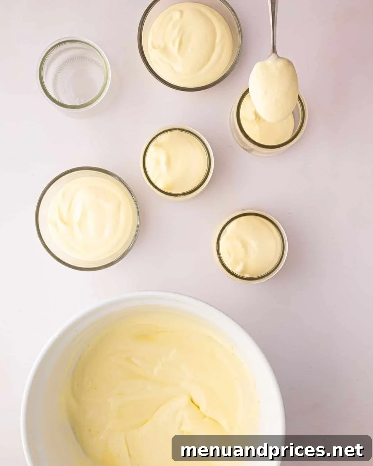 Zesty Lemon Dream 18 A white bowl with thickened lemon mousse. Small glass jars have lemon mousse scooped into them before chilling.