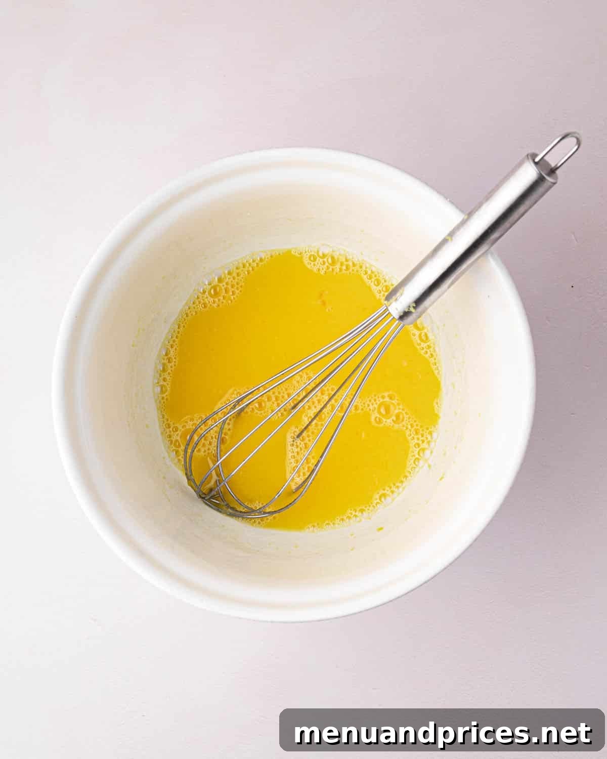 Zesty Lemon Dream 6 A white bowl with lemon juice and egg yolks with a whisk.