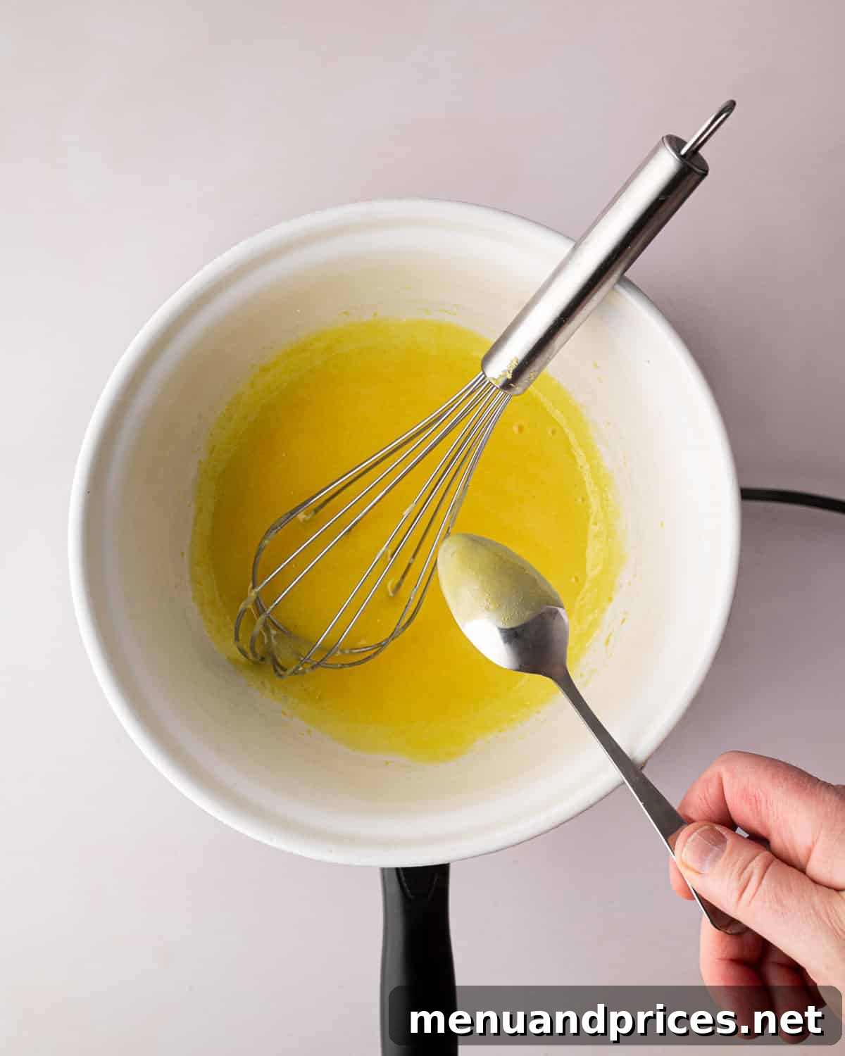 Zesty Lemon Dream 8 A white bowl over a double boiler with thickened egg yolks and lemon juice. A spoon is testing the thickness and a whisk is sitting on the side.