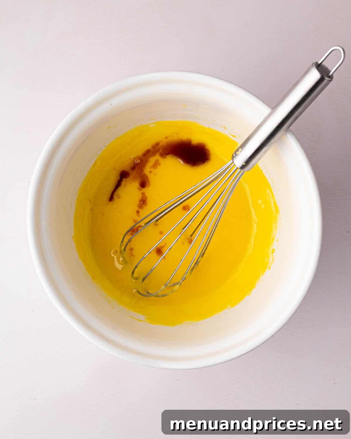 Zesty Lemon Dream 9 A white bowl with the cooked egg yolks and sugar and vanilla extract added. A whisk is resting on the side.