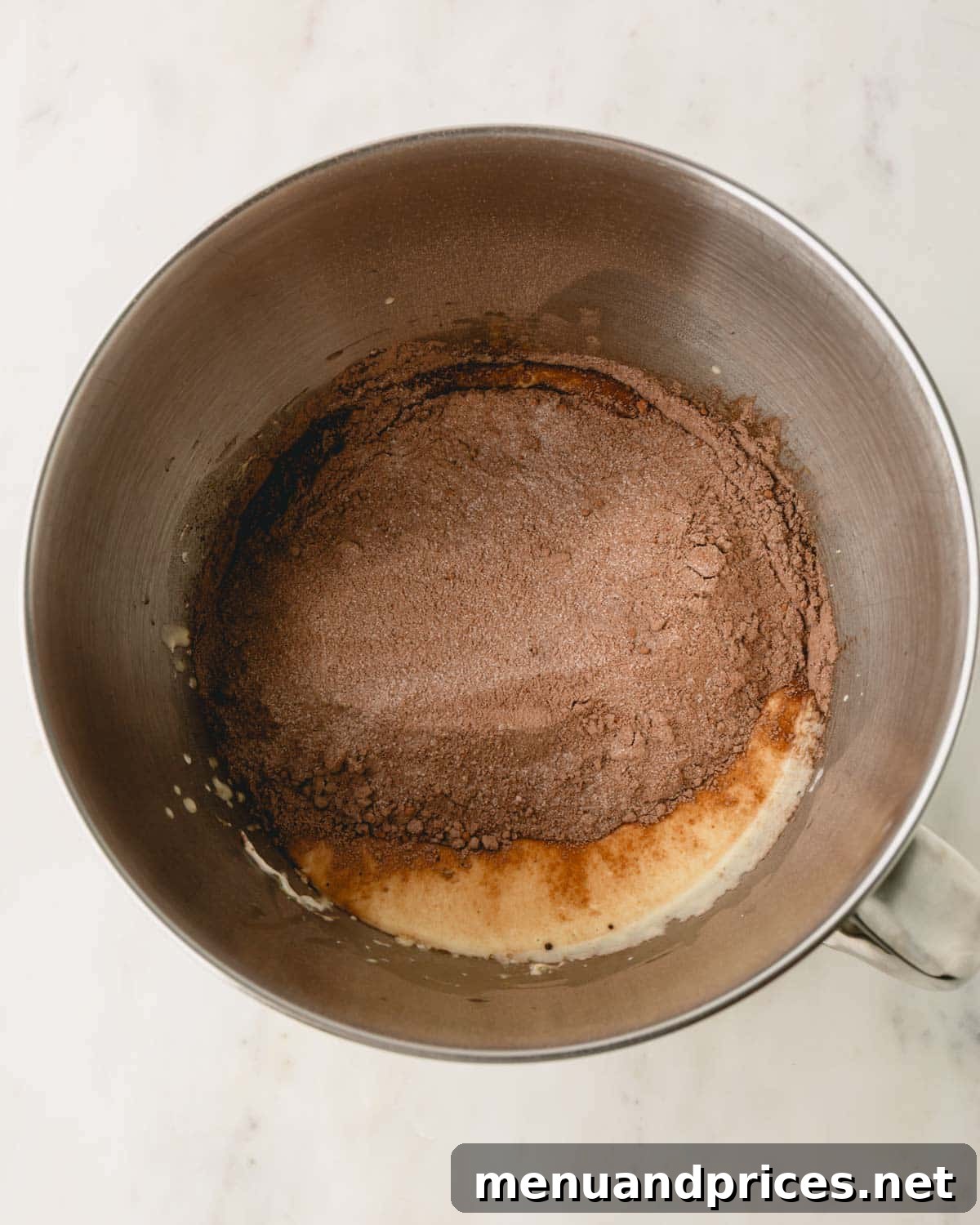 Dry ingredients being added to the wet ingredients in a metal mixing bowl for German chocolate cake batter.