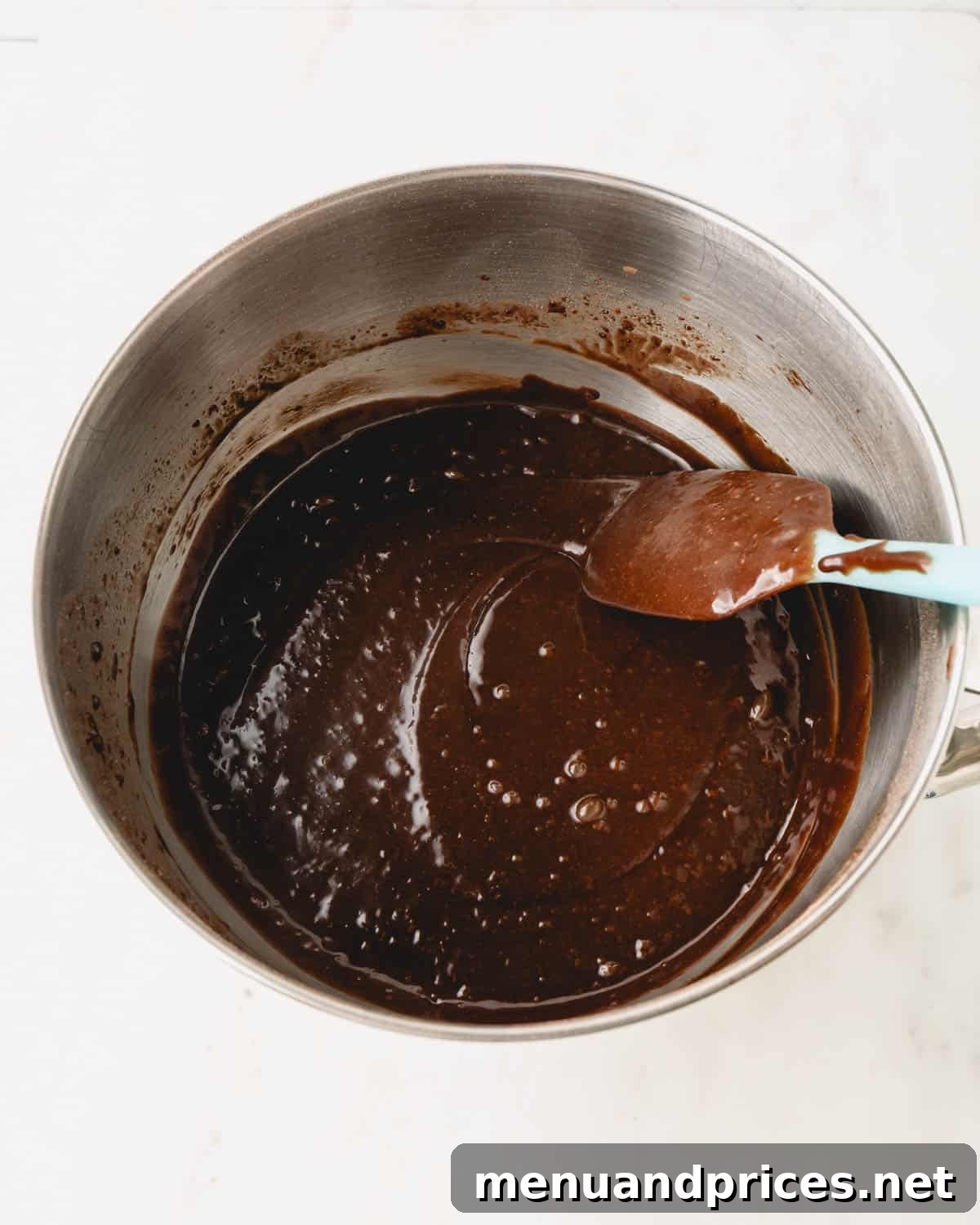 German chocolate cake batter in a metal mixing bowl with a spatula resting on the side, showing its smooth consistency.