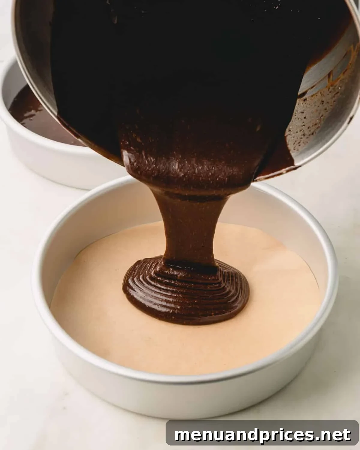 German chocolate cake batter being carefully poured from a stand mixer bowl into a prepared cake pan.