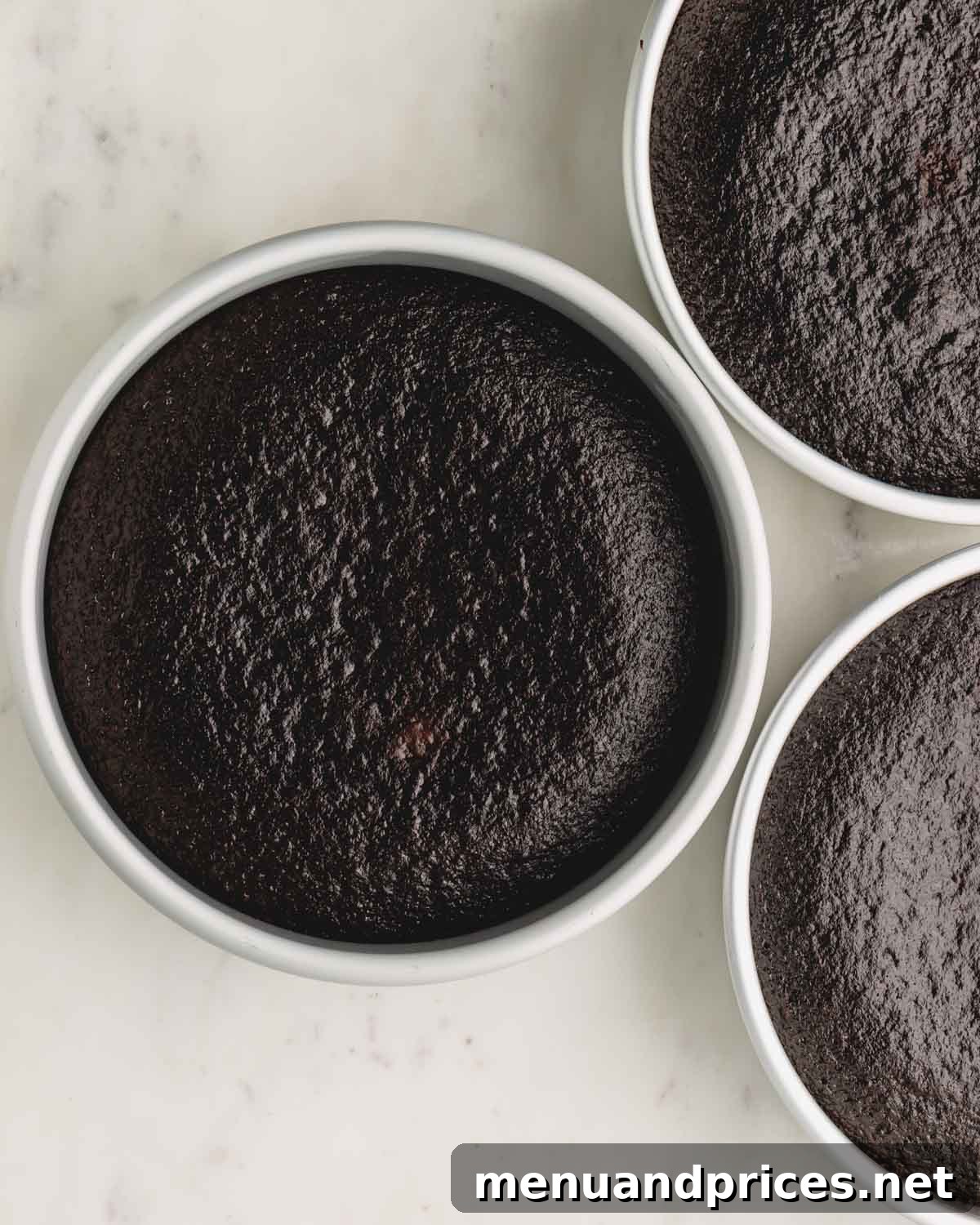 Three golden-brown, freshly baked German chocolate cakes resting in their cake pans on a wire rack.