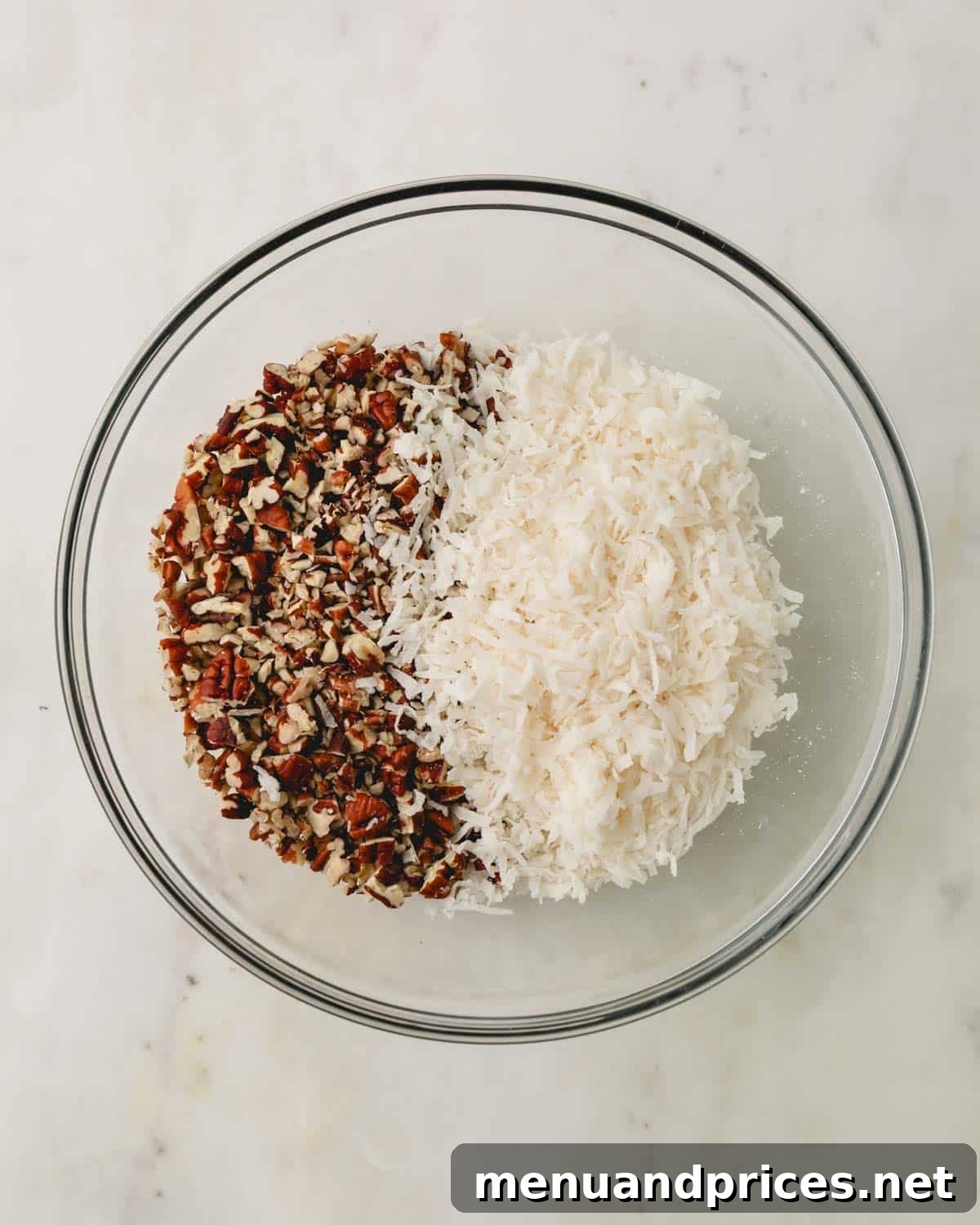 A clear glass bowl filled with separate piles of chopped pecans and sweetened coconut flakes.