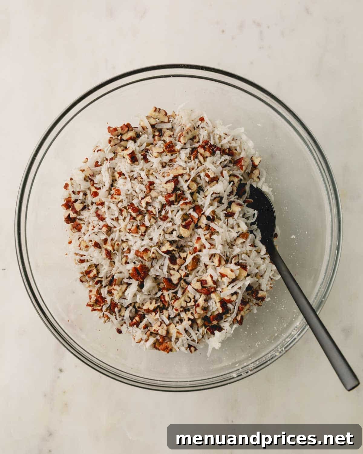 A clear glass bowl containing chopped pecans and sweetened coconut flakes, mixed evenly together.