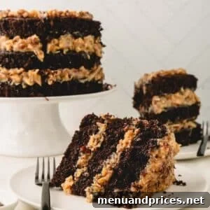 A slice of German chocolate cake on a white plate with a cake on a pedestal and another slice in the background.