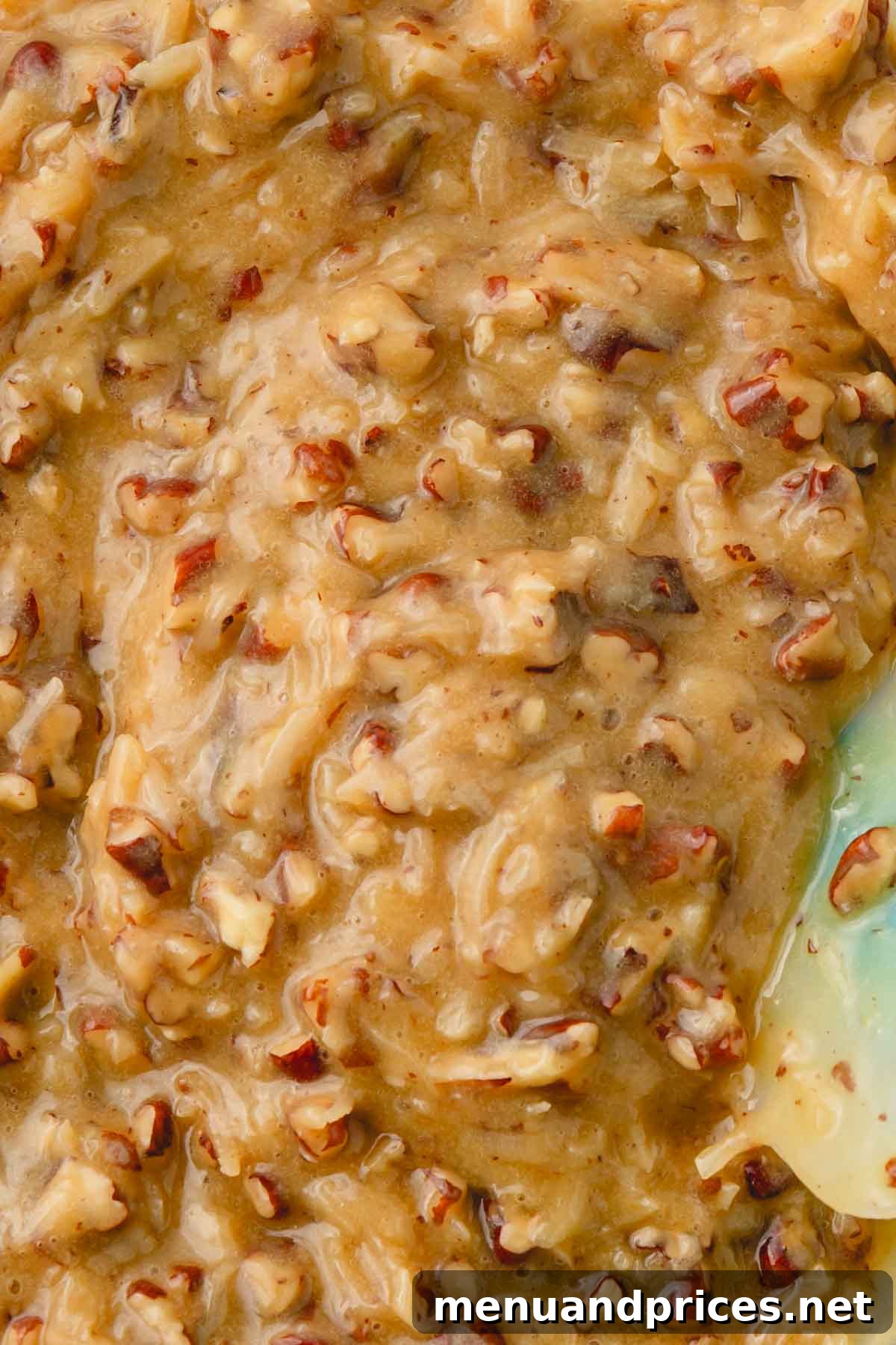 A close-up image showing the thick, creamy, and textured caramel pecan frosting, speckled with toasted pecans and shredded coconut.