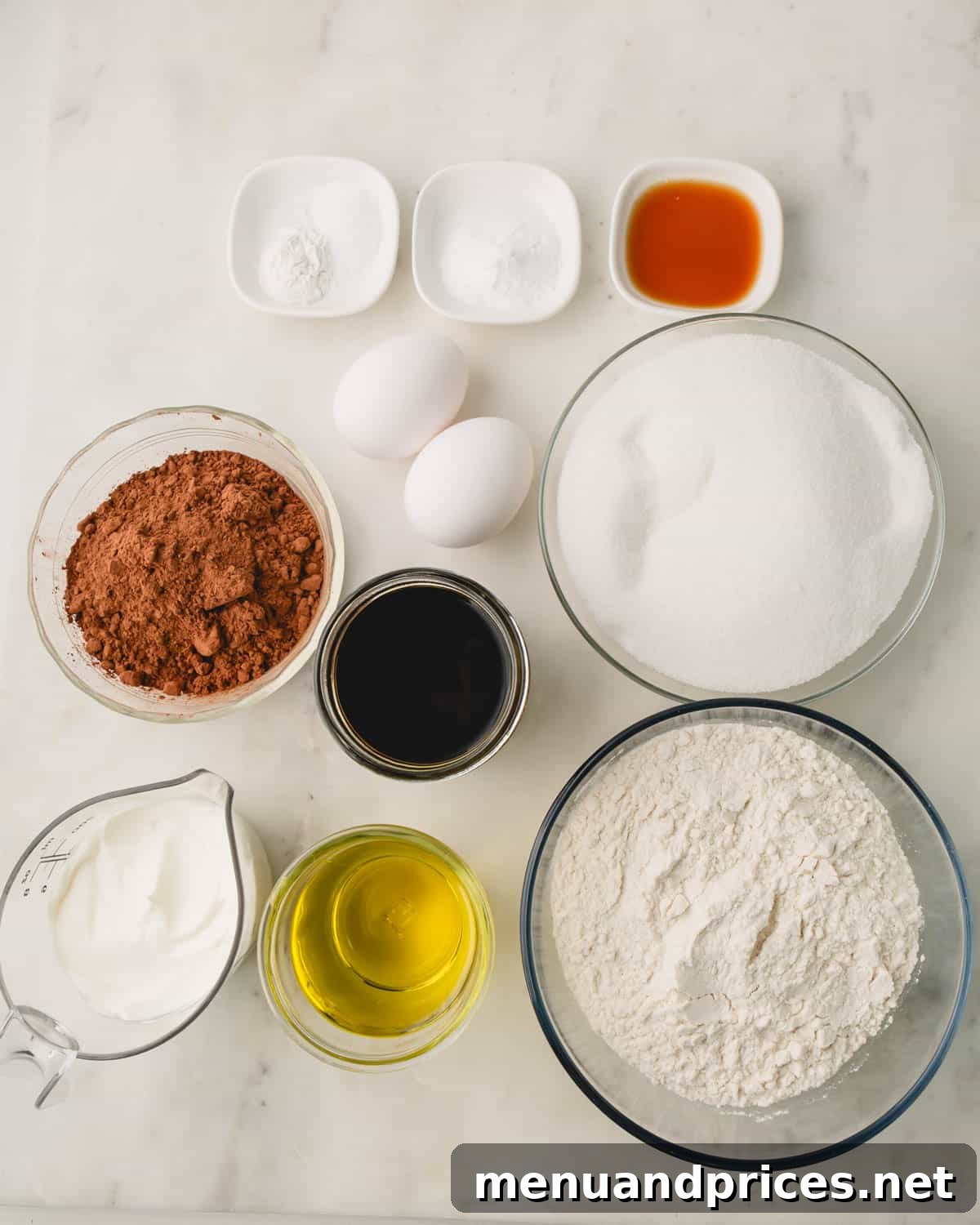 A selection of ingredients for German chocolate cake displayed on a counter, including flour, cocoa powder, eggs, and sour cream.