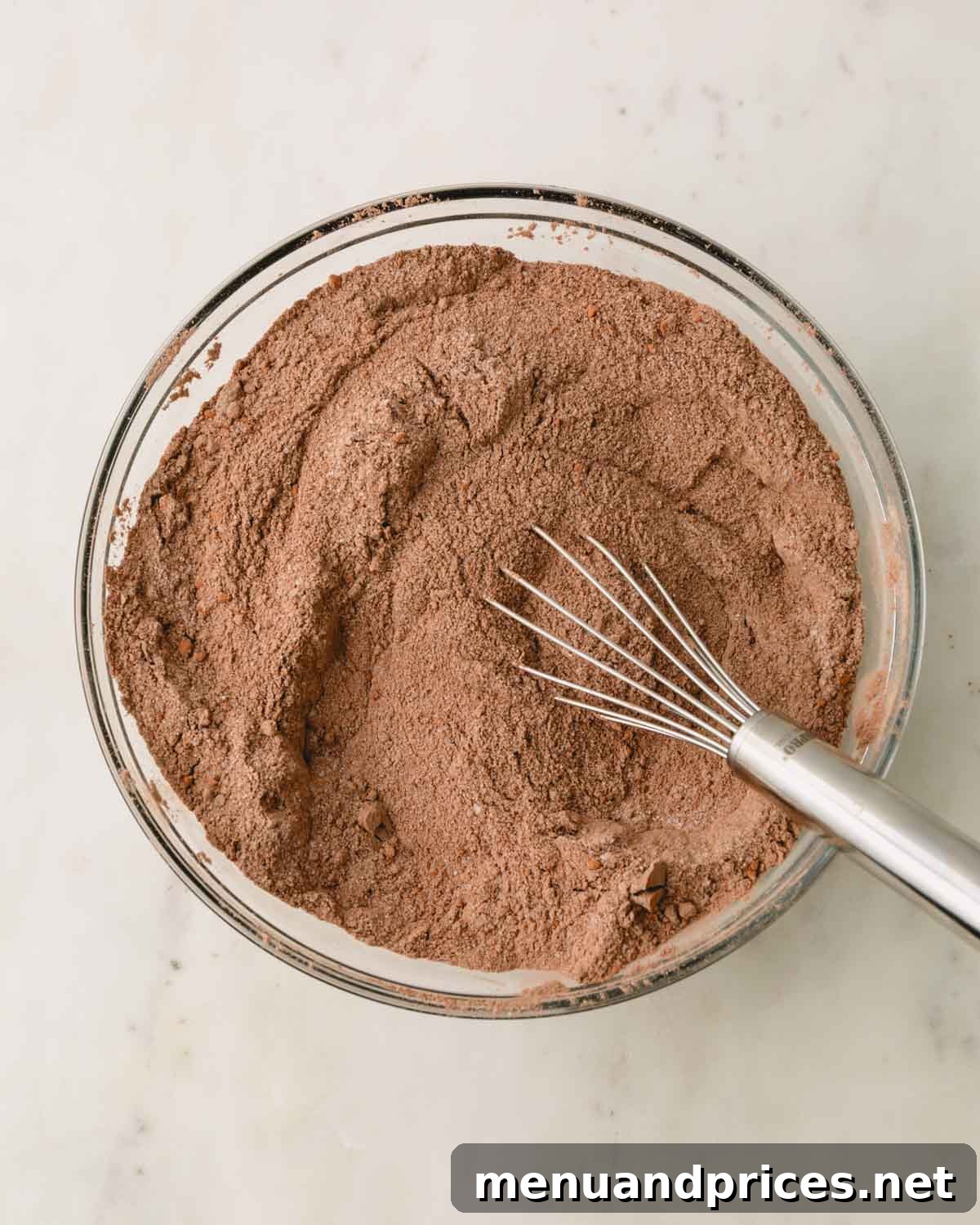A glass bowl with the dry ingredients for German chocolate cake already whisked together, showing a uniform dark brown color.